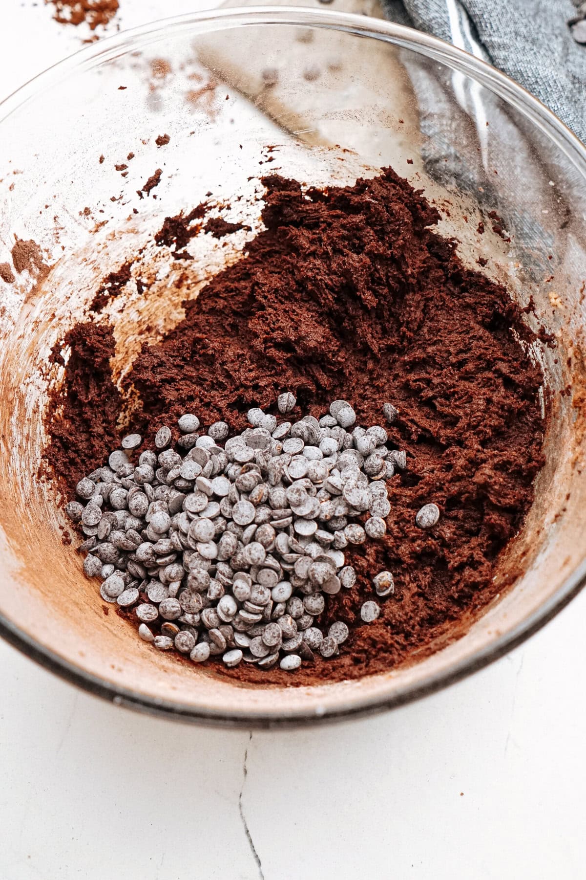 A glass bowl containing chocolate cookie dough and a pile of chocolate chips.