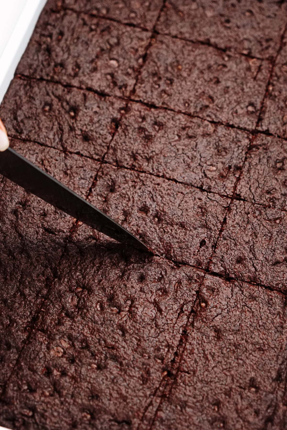 A knife cuts into a tray of freshly baked, evenly sliced brownies.