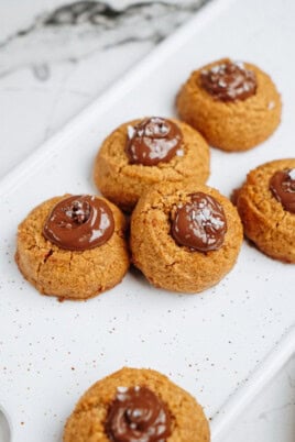 Peanut Butter Thumbprint Cookies topped with chocolate and a sprinkle of salt, arranged on a speckled white platter.