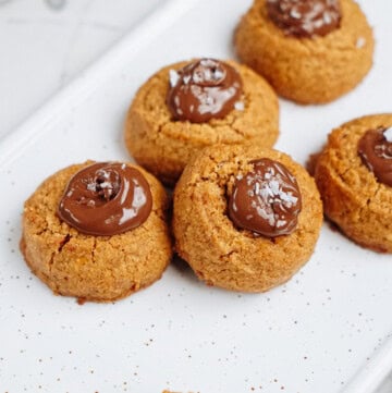 Peanut Butter Thumbprint Cookies topped with chocolate and a sprinkle of salt, arranged on a speckled white platter.