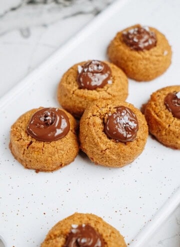 Peanut Butter Thumbprint Cookies topped with chocolate and a sprinkle of salt, arranged on a speckled white platter.