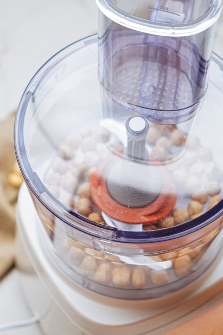 A food processor with a transparent lid containing chickpeas, ready for processing.