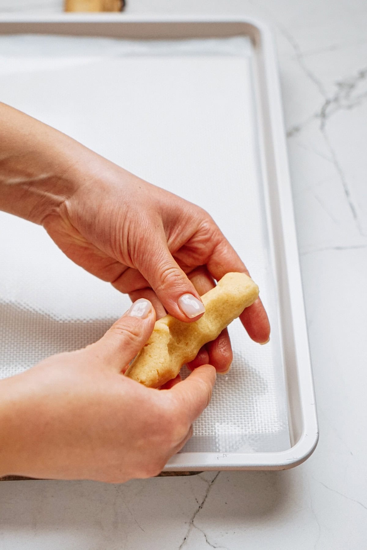 Hands shaping dough on a baking sheet lined with parchment paper.