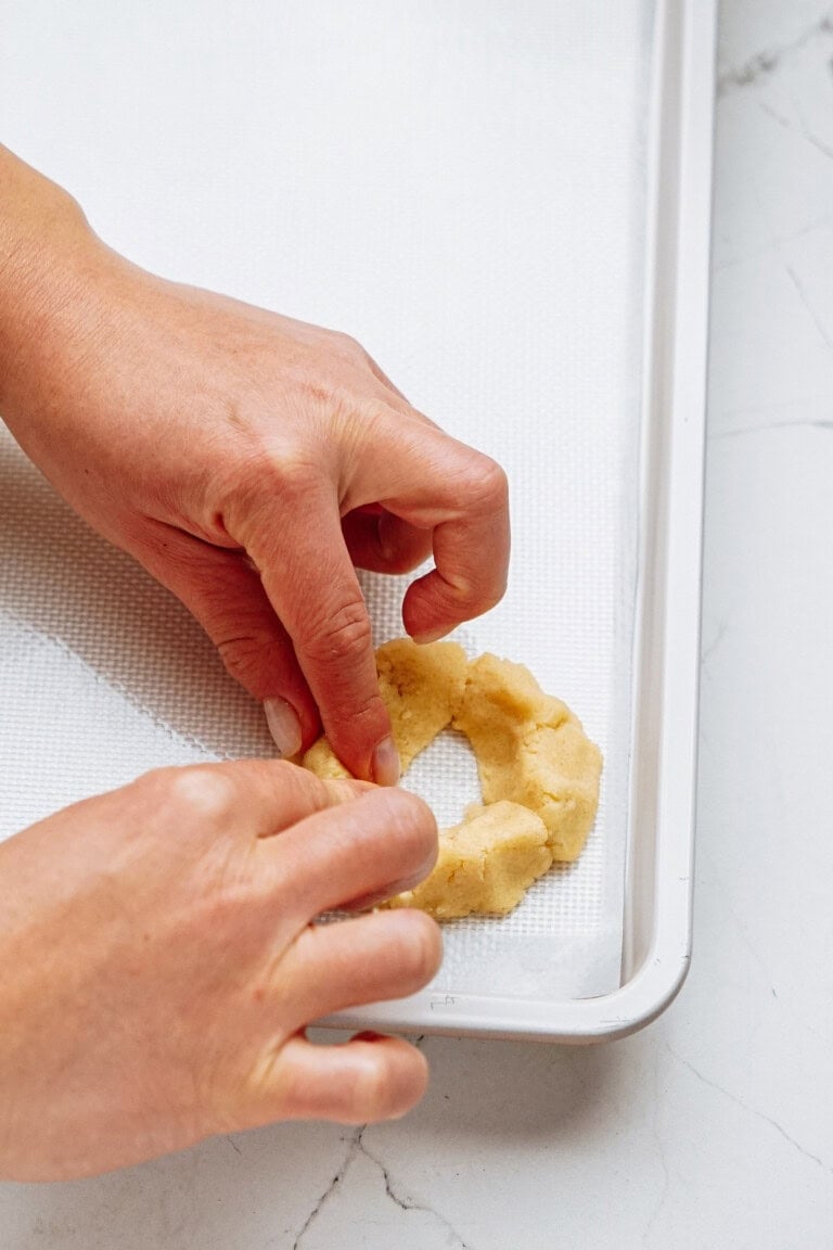 Hands shaping dough into a ring on a baking sheet lined with parchment paper.