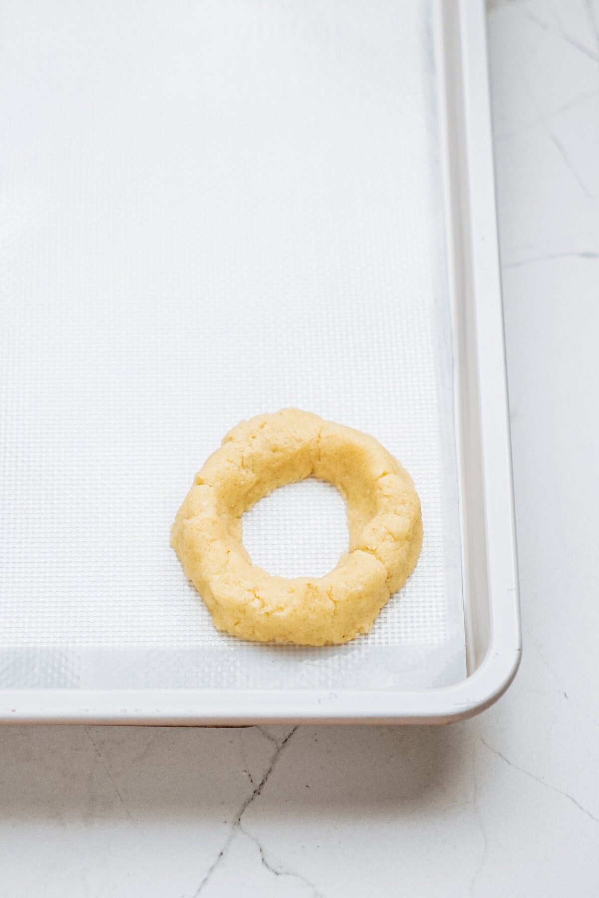 A single unbaked cookie dough ring on a lined baking tray.