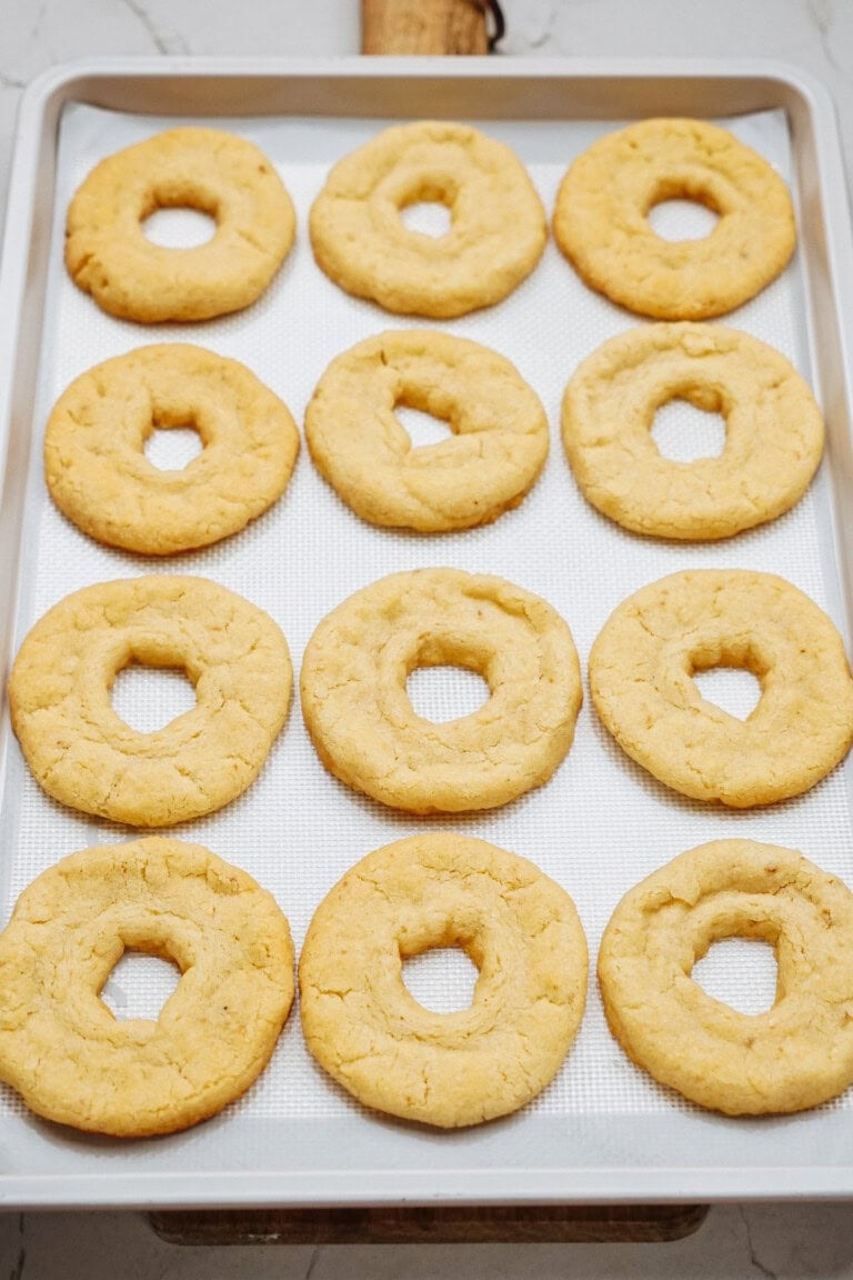 Twelve round cookies with holes in the center, arranged in rows on a baking sheet lined with parchment paper.