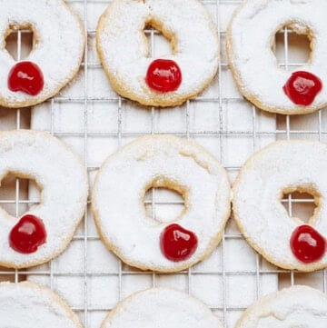 Round cookies with white icing and a red cherry on top are arranged on a cooling rack.