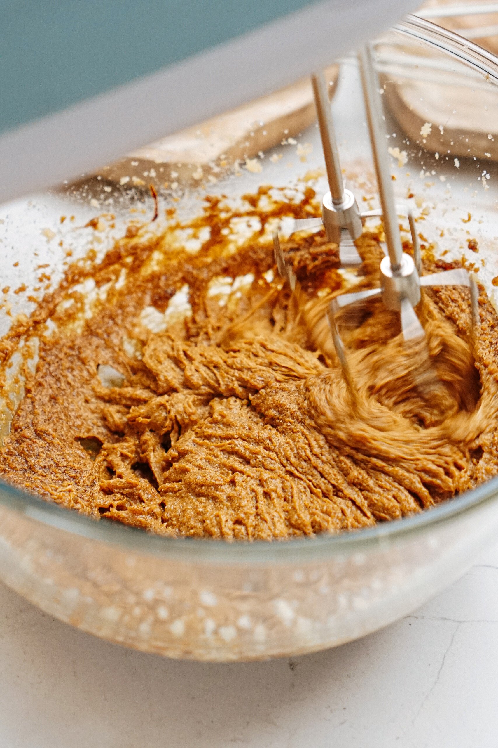 The electric mixer whirrs, seamlessly blending the brown cookie dough for delicious gingerdoodle sandwich cookie in a glass bowl.