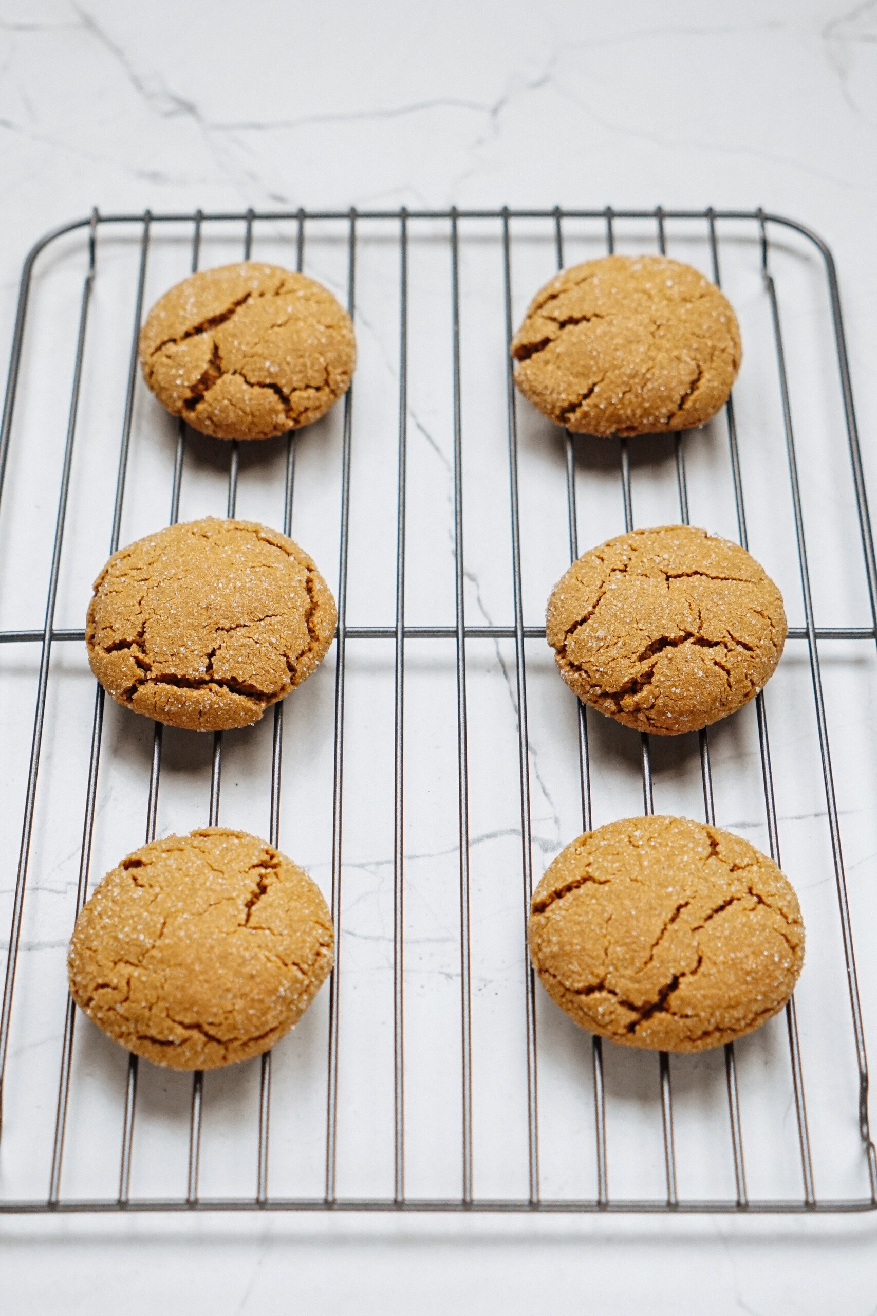 Six round cookies rest on a cooling rack, placed on a white marble countertop.