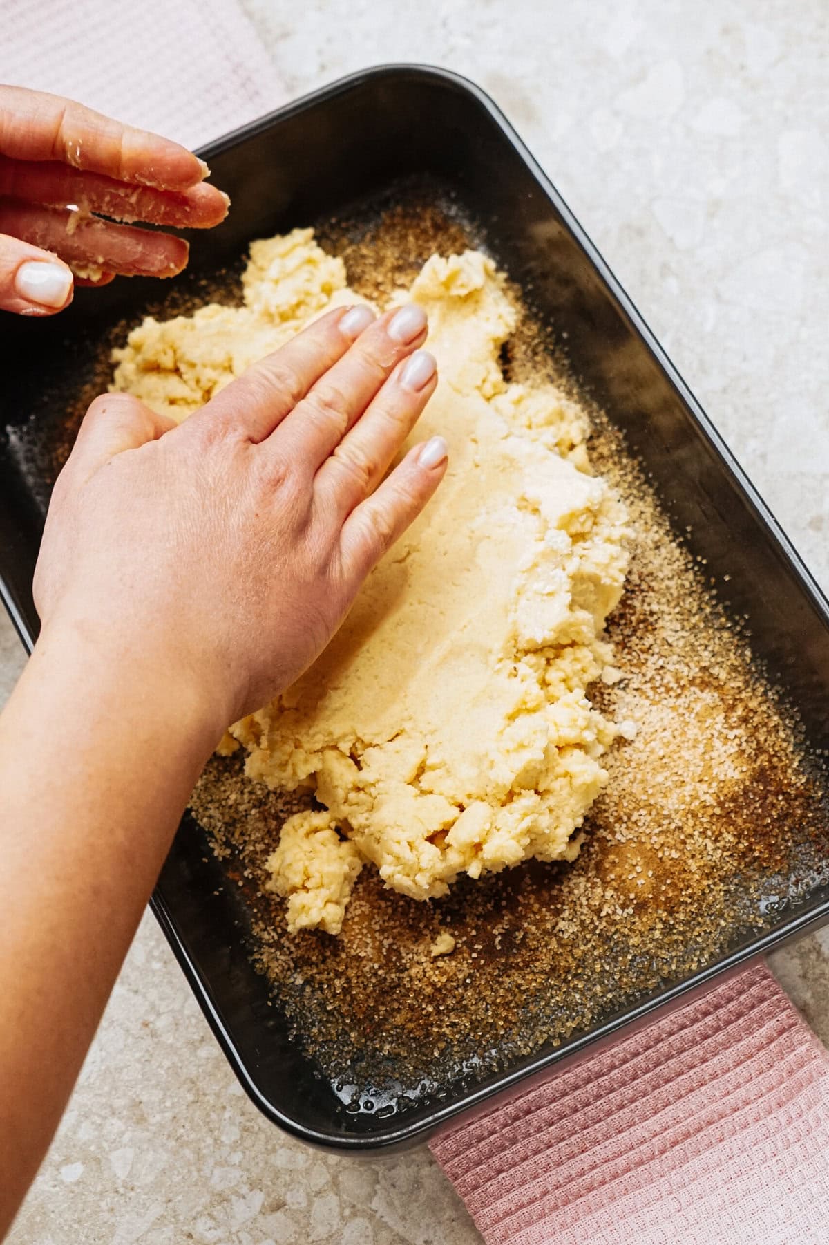 Hands pressing dough into a rectangular baking pan lined with breadcrumbs.