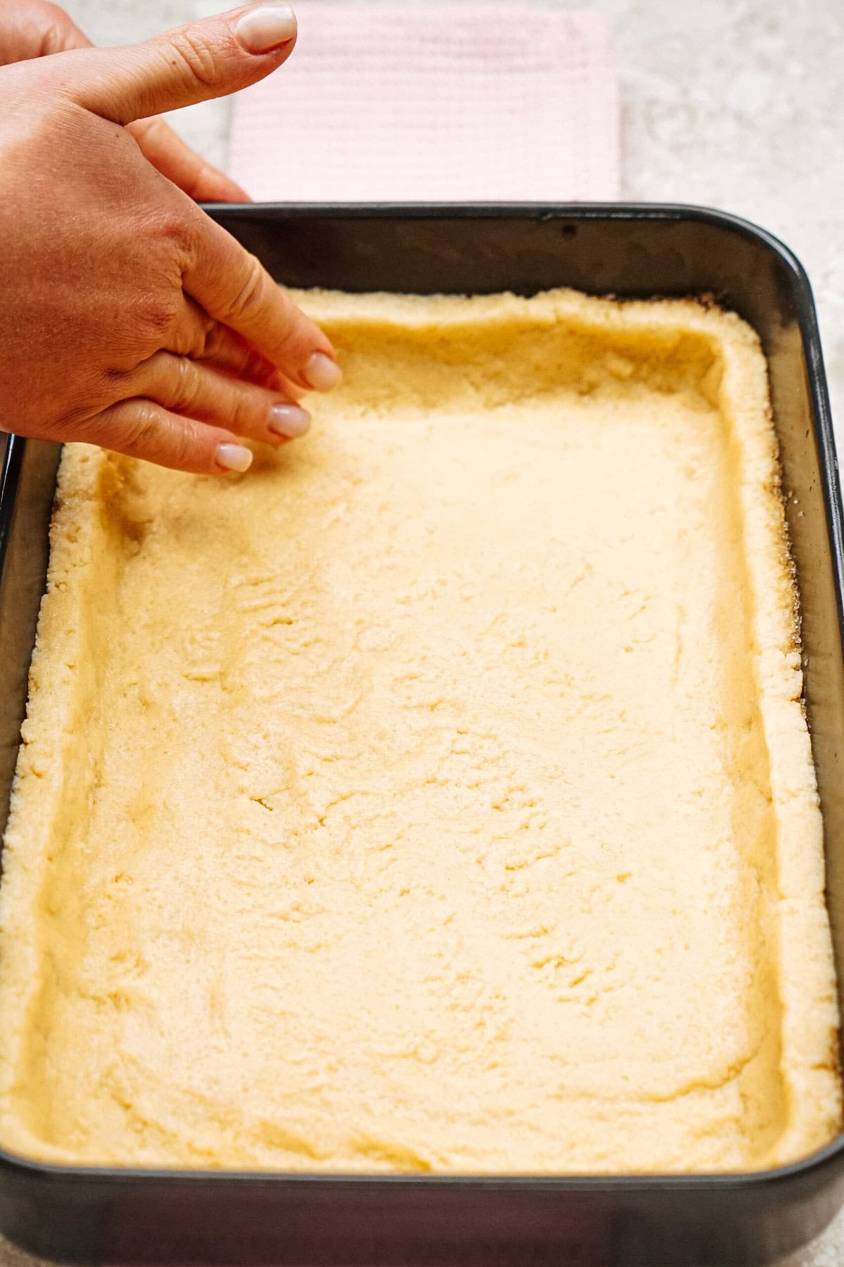 Person pressing dough into a rectangular baking dish.