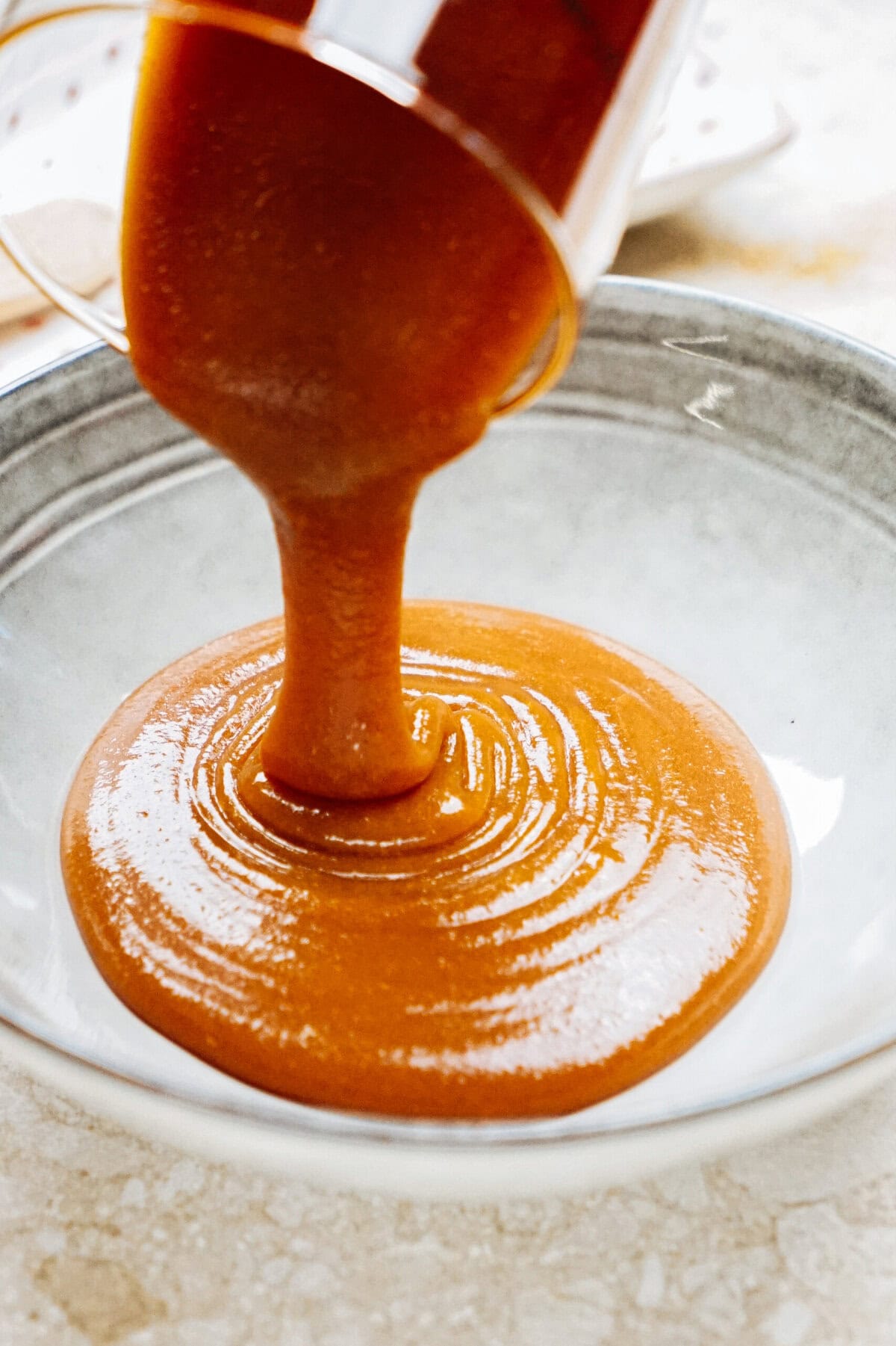 Thick orange-brown sauce being poured from a container into a gray bowl.