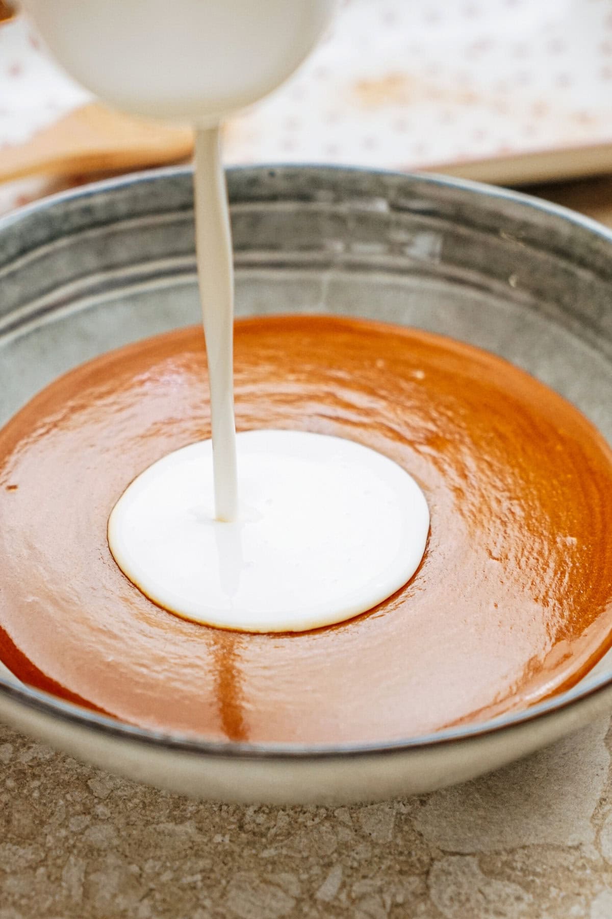 Pouring white cream onto a bowl of brown soup on a table.