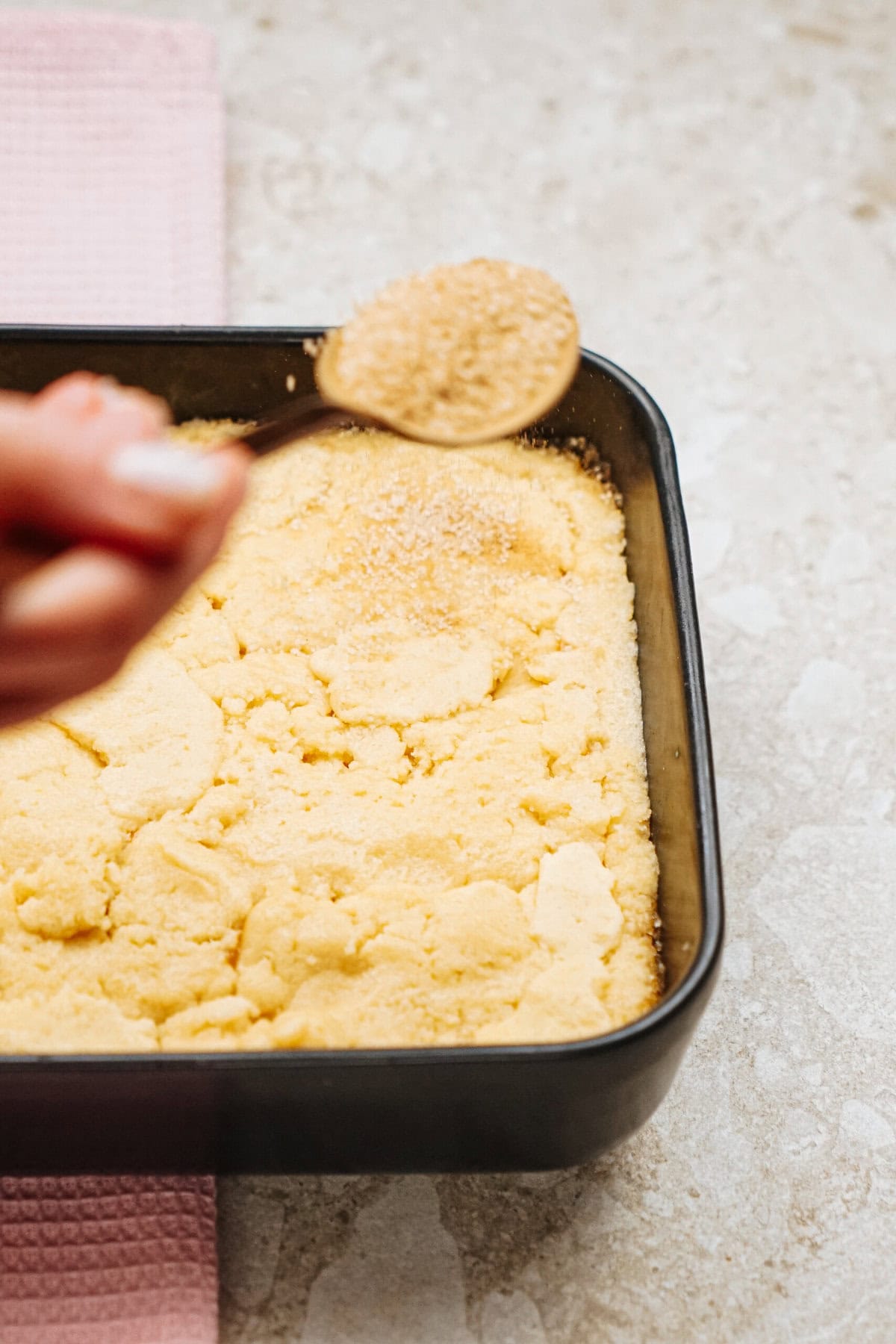 A hand holding a spoon sprinkles sugar over a tray of unbaked dough.