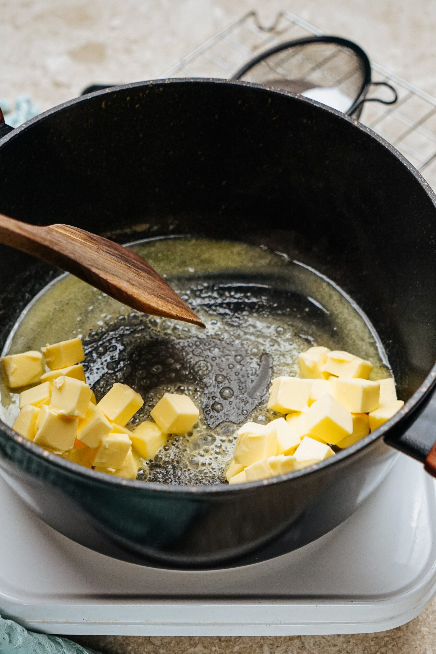 Cubes of butter melting in a black pot with a wooden spoon on a stove.