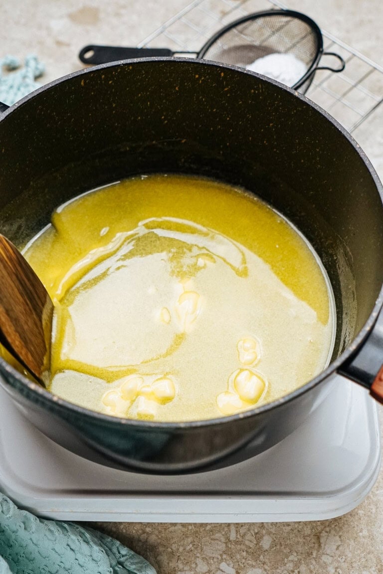 A pot with melted butter being stirred by a wooden spoon, placed on a stovetop.