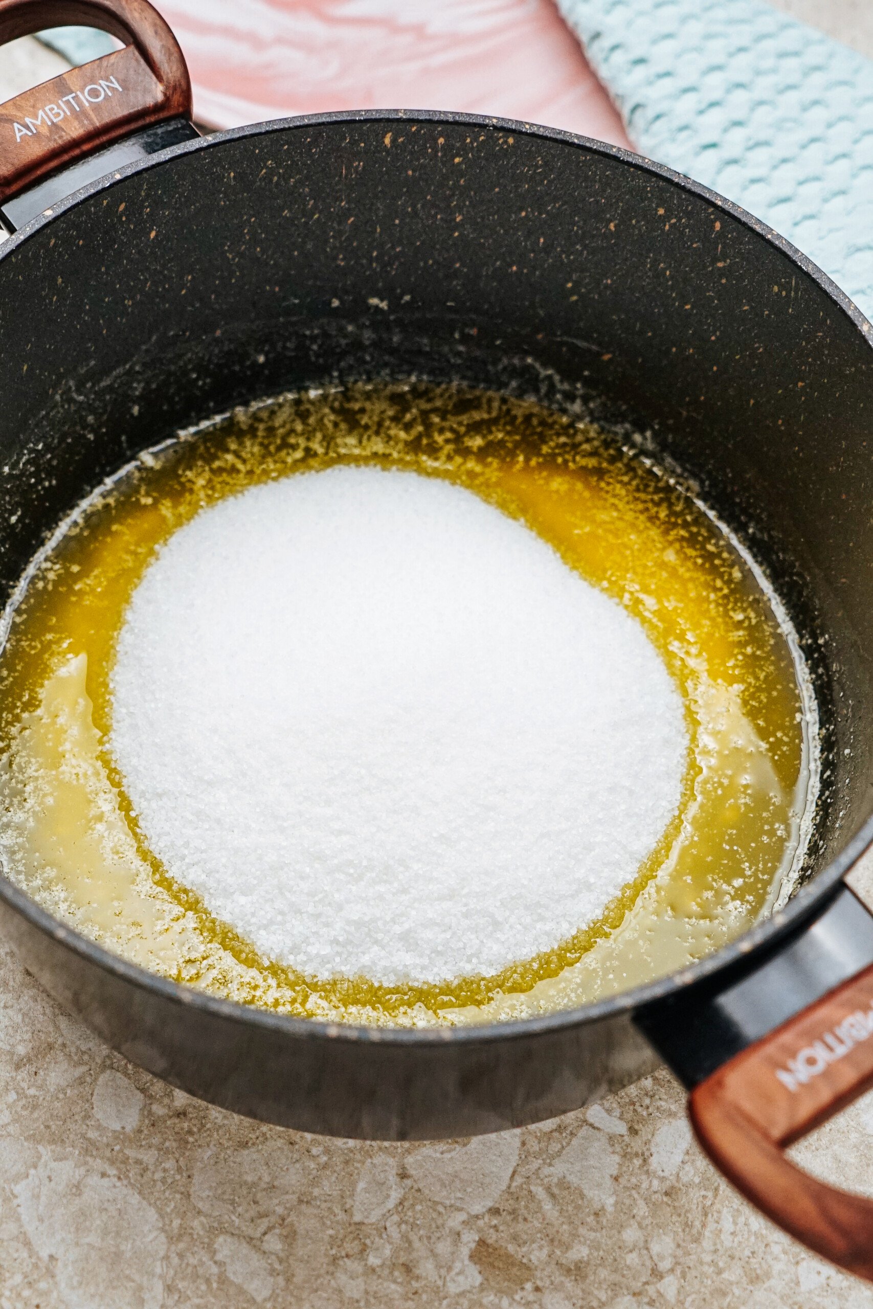 A pot filled with melted butter and a mound of sugar on top, placed on a light-colored textured surface.