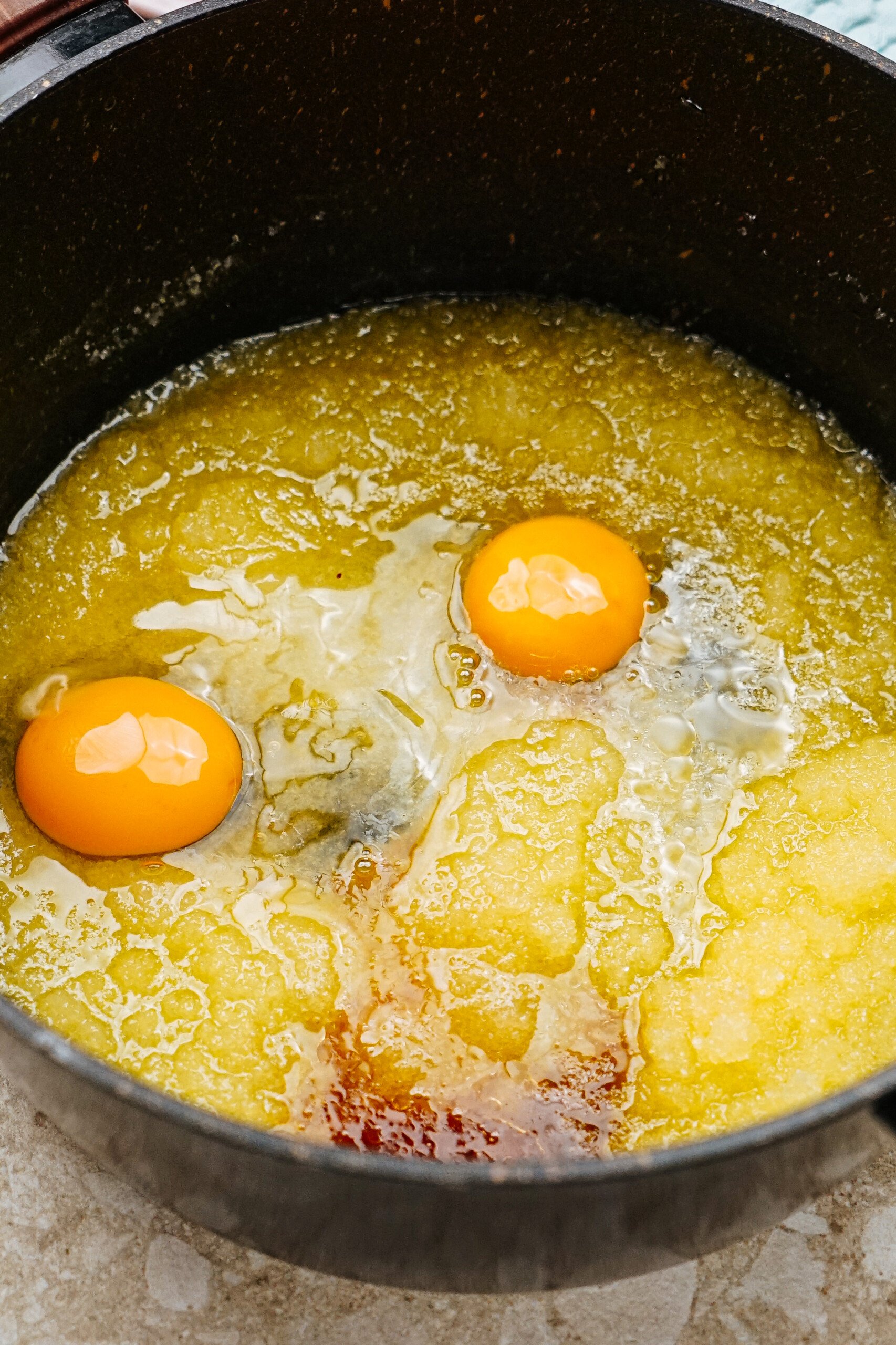 Two raw eggs on top of a mixture in a black pot, likely for baking or cooking.