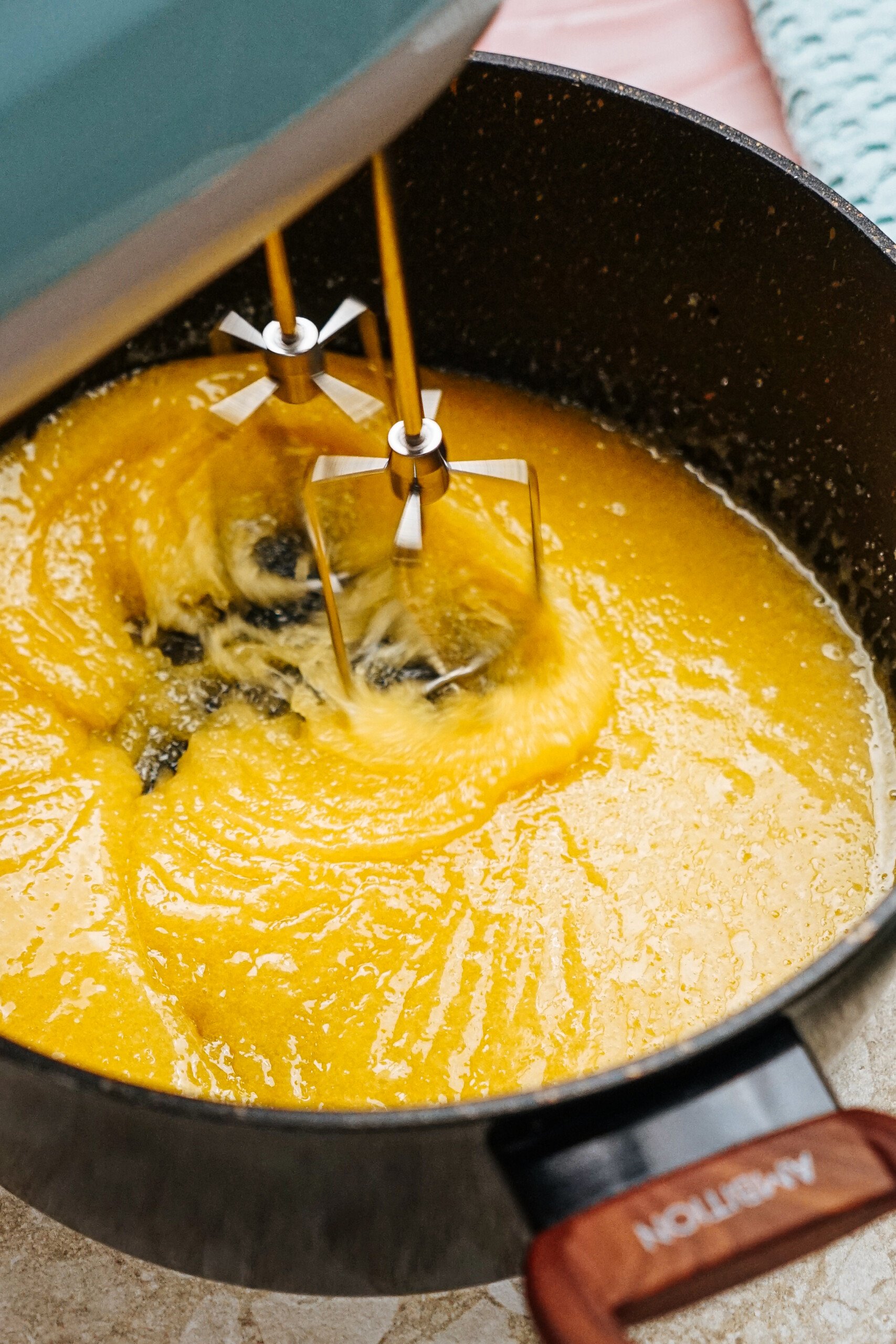 A mixer combines a yellow batter in a black pot on a kitchen countertop.