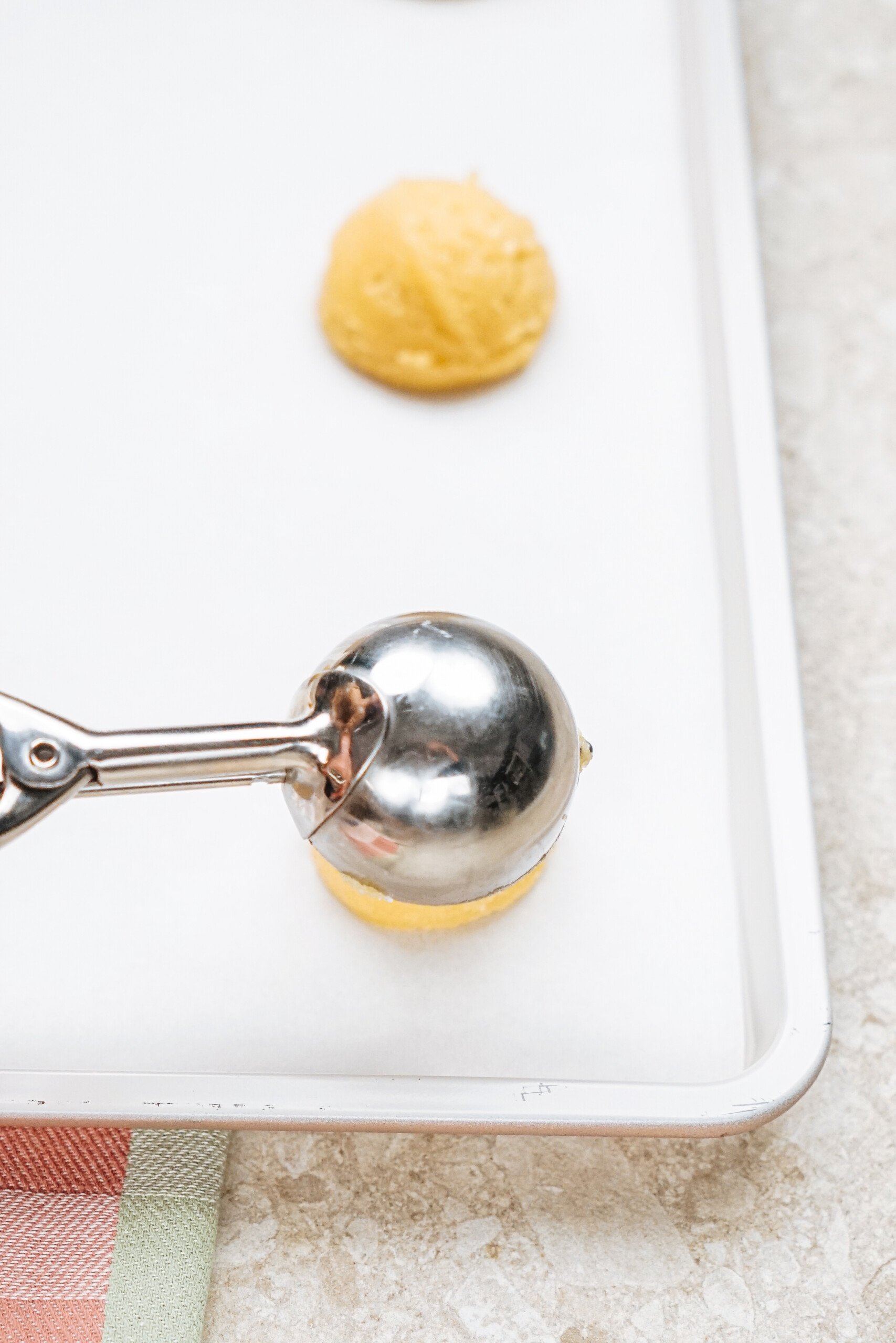 Ice cream scooper with dough on a baking sheet, ready for baking.