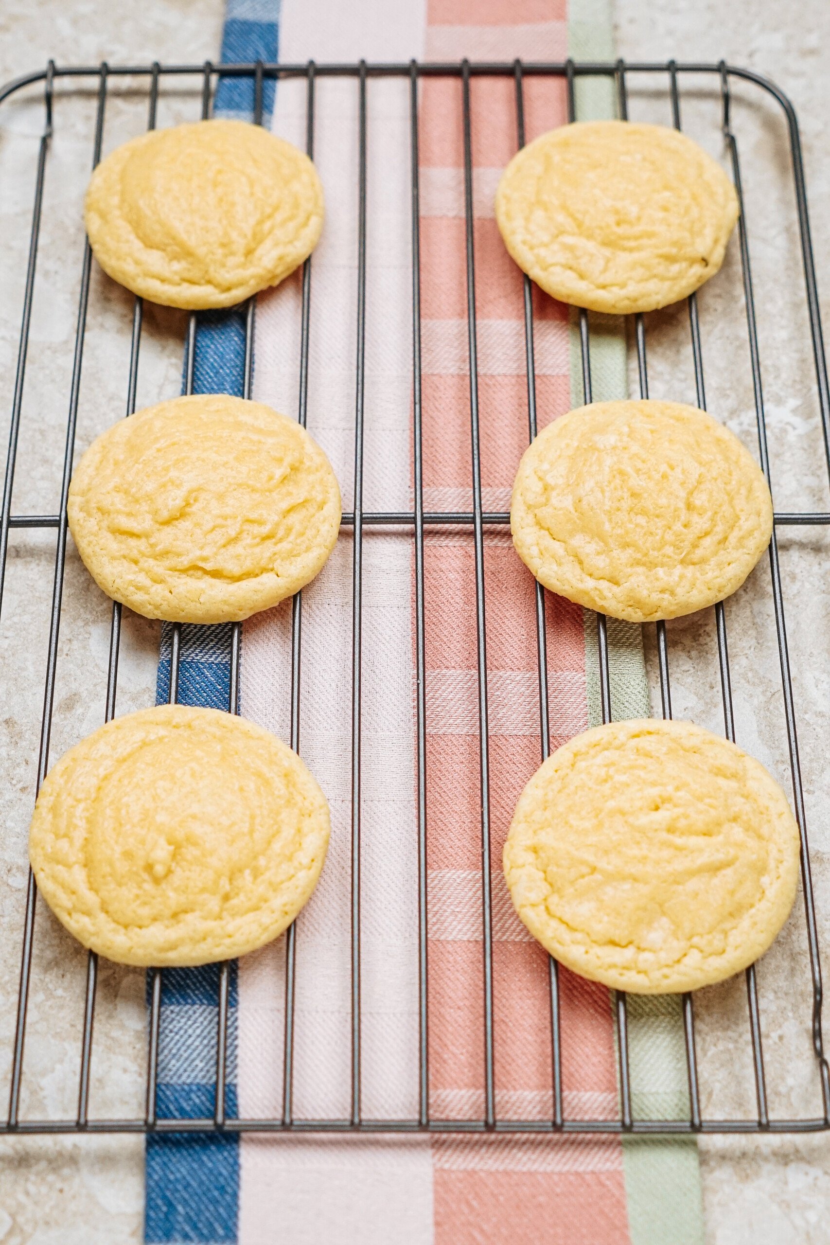 Six sugar cookies cooling on a wire rack with a colorful striped cloth underneath.