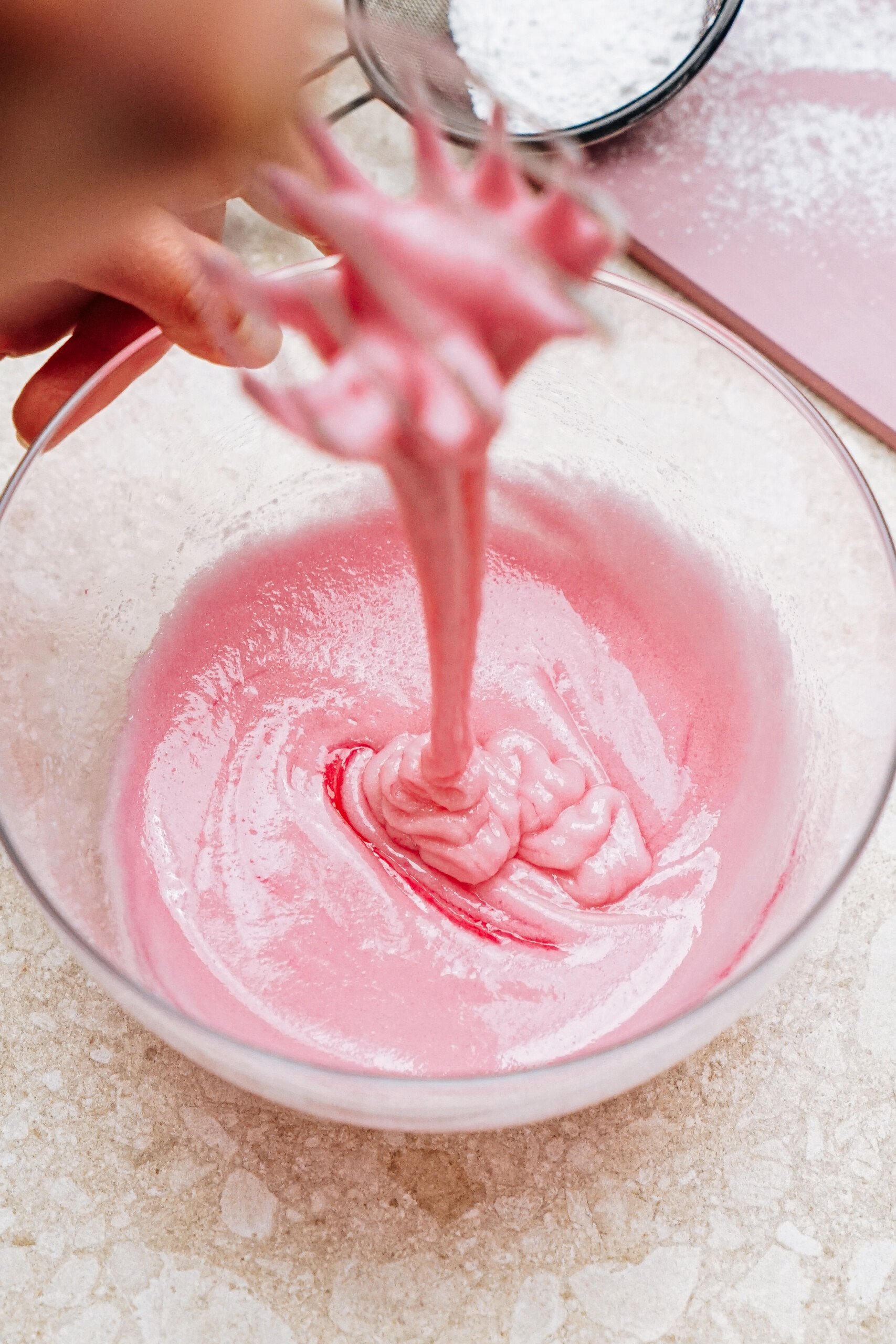 A person mixing pink batter in a glass bowl with a whisk.