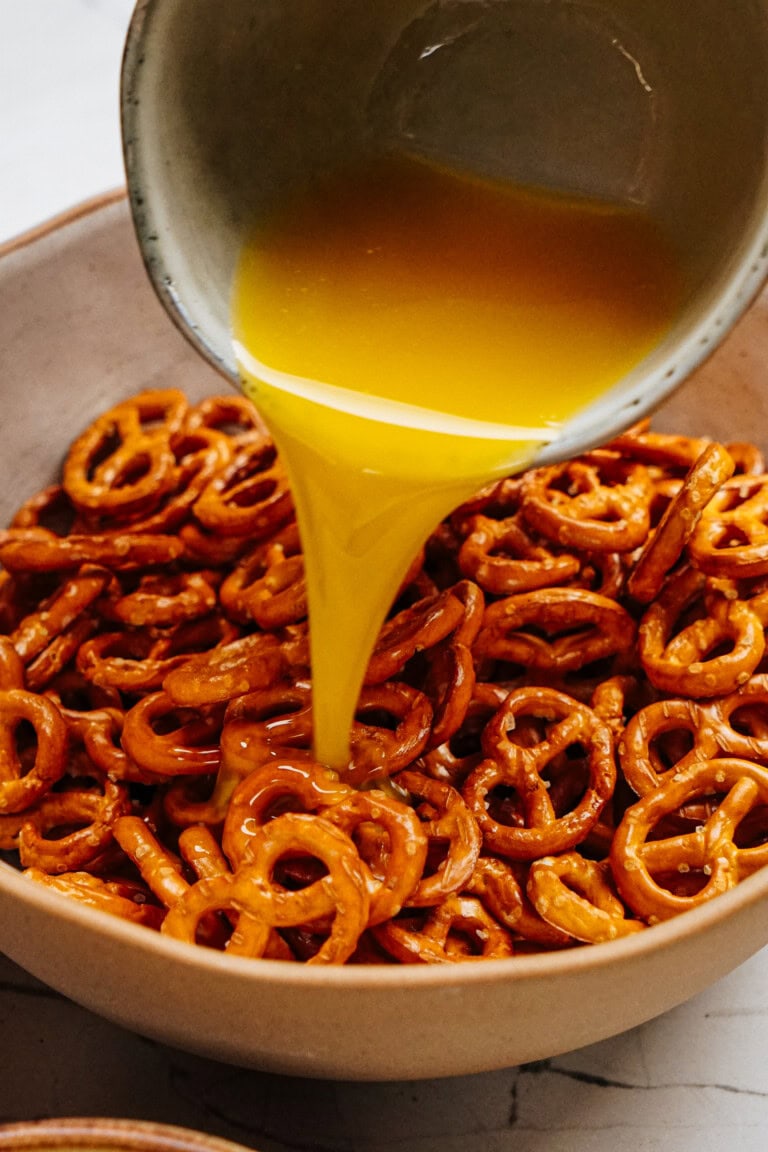 A bowl of pretzels is being drizzled with melted butter from a pouring cup, reminiscent of cinnamon roll pretzels.