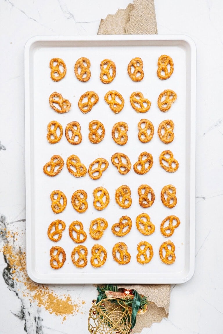 A baking sheet with evenly spaced cinnamon roll pretzels rests on parchment paper, set on a marble countertop.