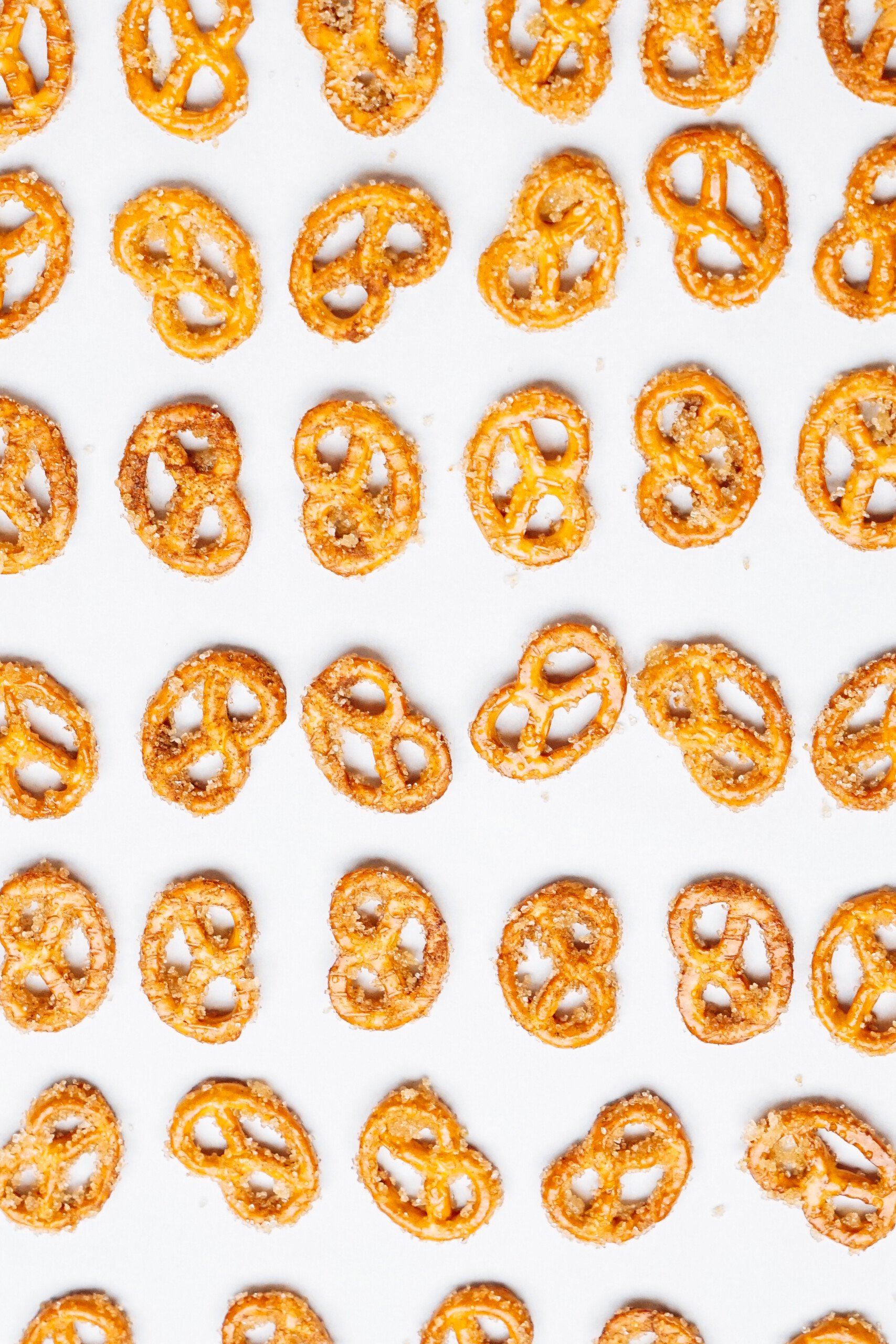 A pattern of cinnamon roll pretzels arranged in rows on a white surface.