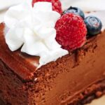 A slice of chocolate cake topped with whipped cream, raspberries, and blueberries on a plate.