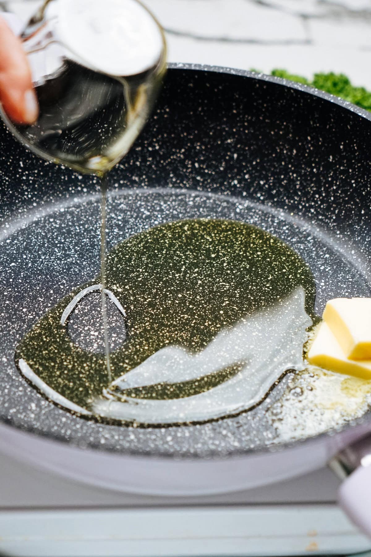 Oil and a pat of butter melt in a non-stick frying pan, ready to create the perfect base for your chicken and kale pasta.