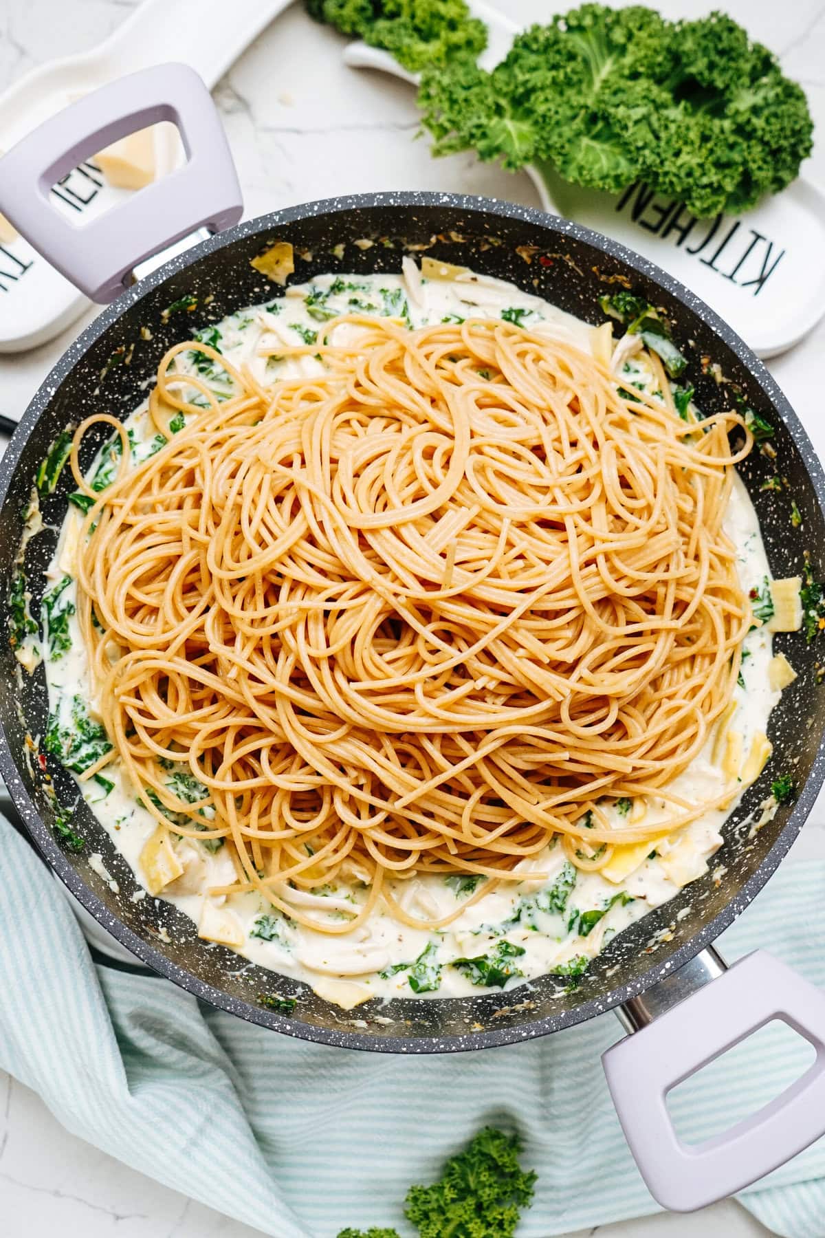 A pot of delicious pasta on top of a creamy sauce with spinach, tender pieces of chicken, and artichoke.