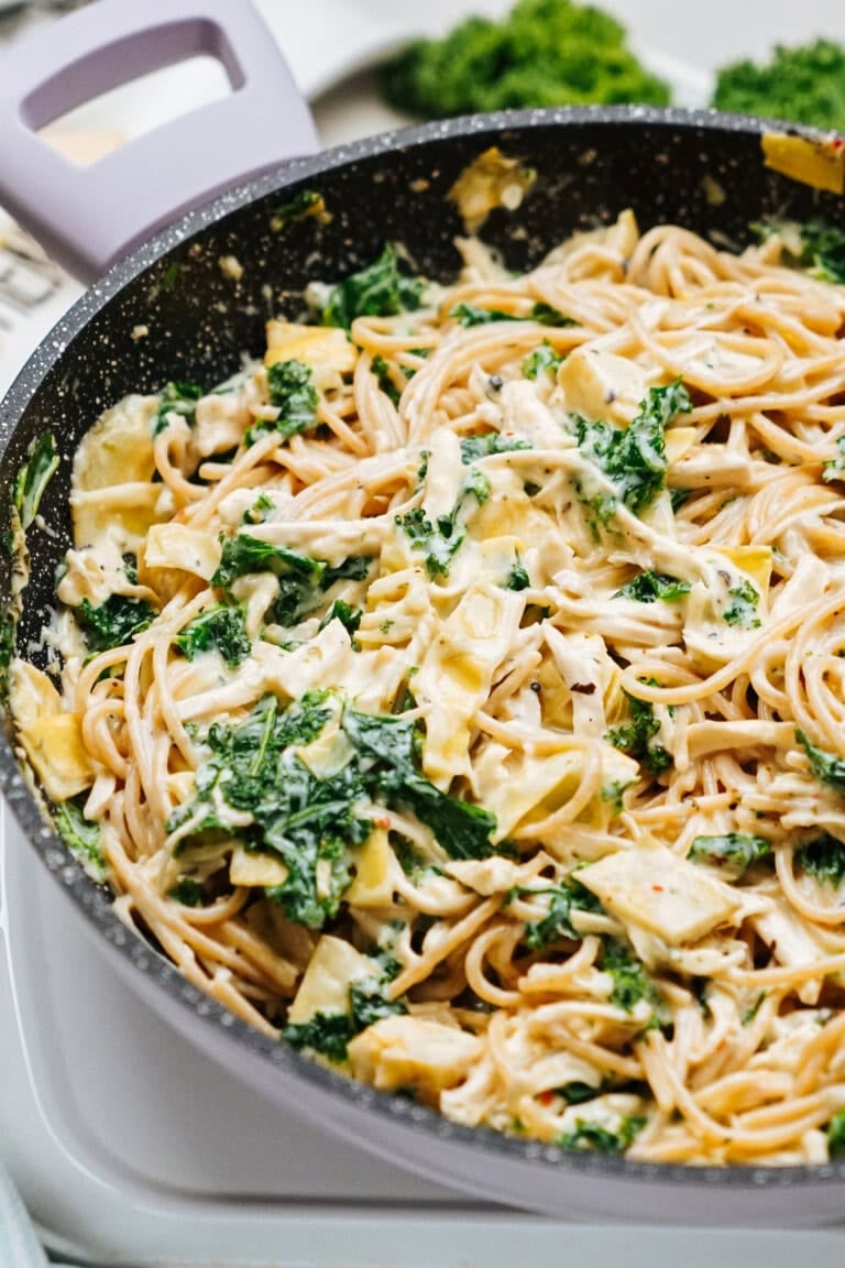 A skillet filled with chicken, spaghetti, kale, and a creamy sauce.