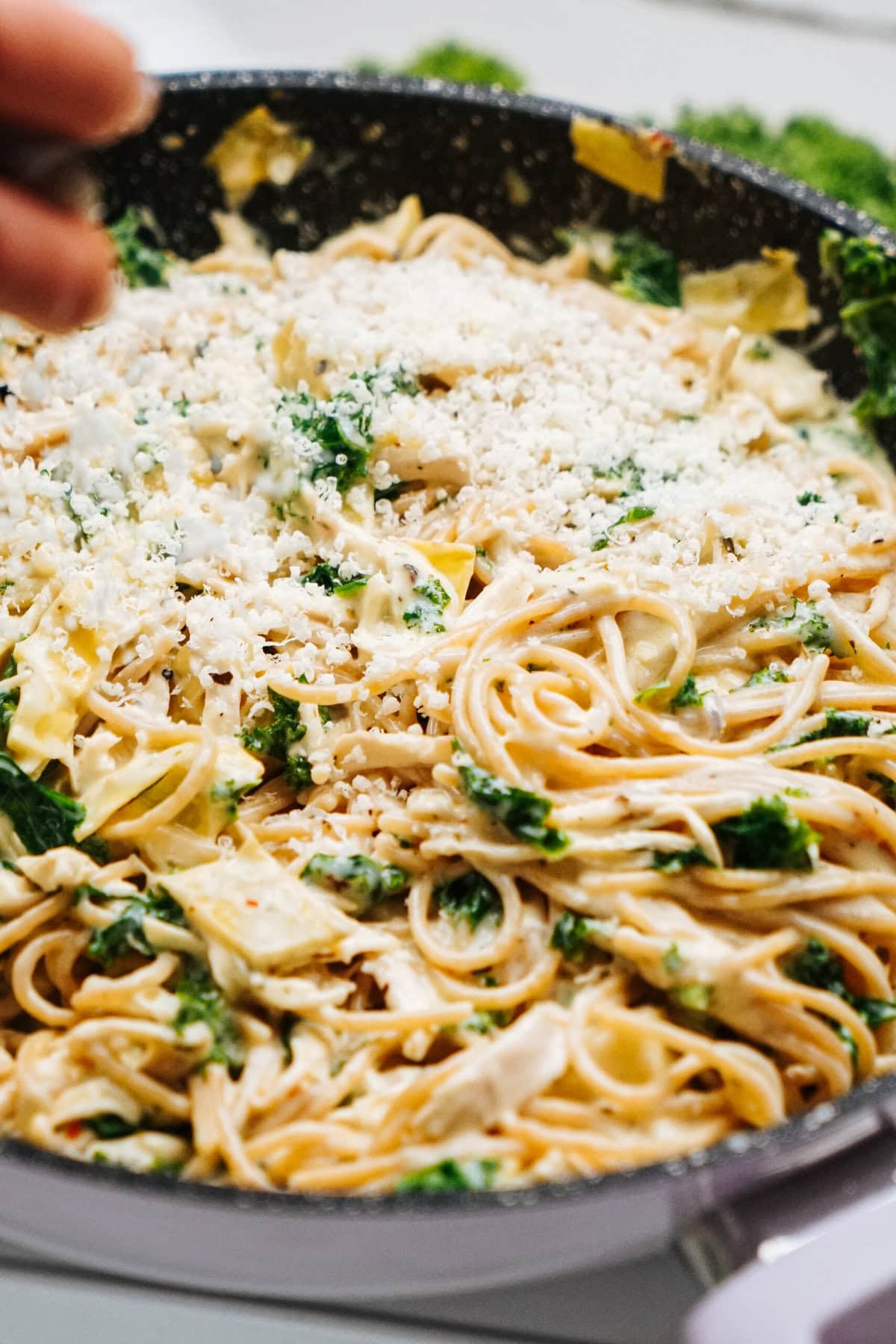 Spaghetti with creamy sauce, chicken, kale, and cheese in a pan, being stirred with a wooden spoon.