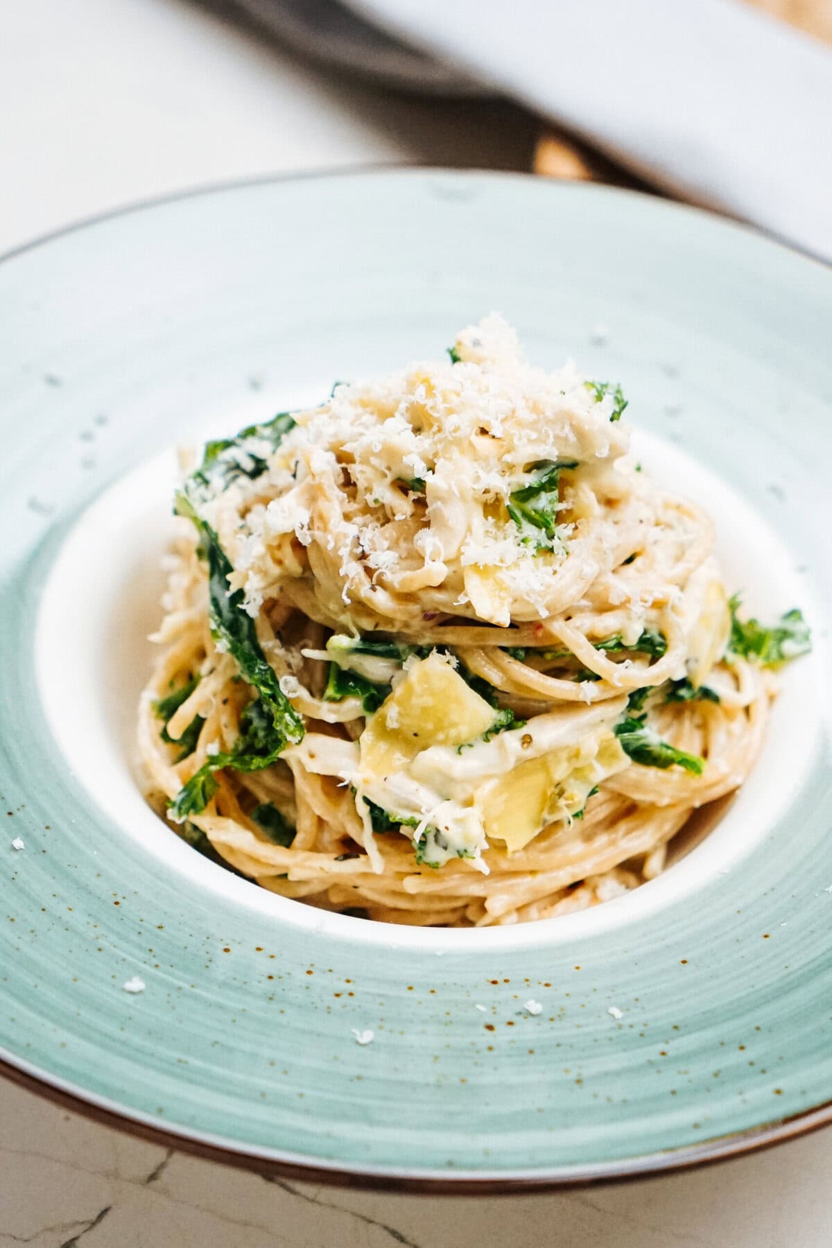 A plate of creamy chicken kale pasta topped with grated cheese and green vegetables, served on a green-rimmed white plate.