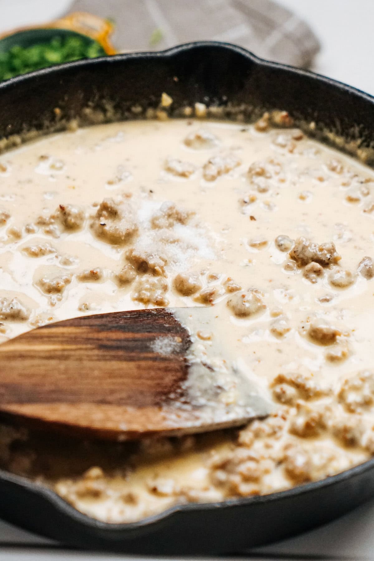 A skillet with creamy Sausage Alfredo gravy and a wooden spatula.