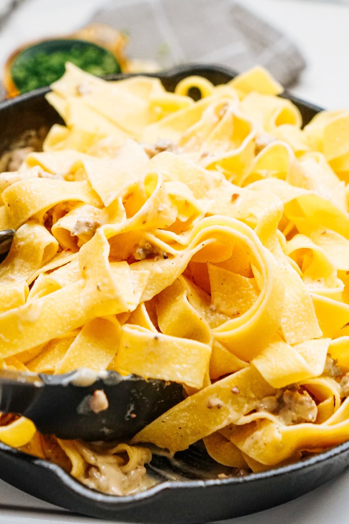 A skillet filled with wide pasta noodles mixed with a creamy Alfredo sauce and small chunks of sausage.