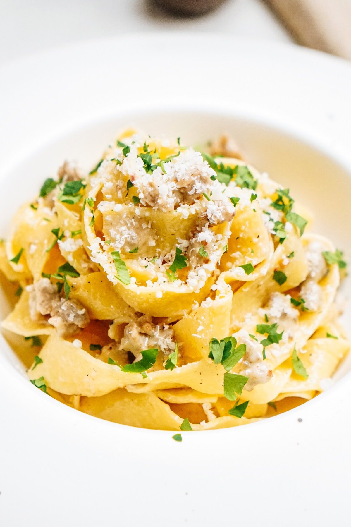 A plate of Sausage Alfredo pasta topped with crumbled sausage, grated cheese, and chopped parsley.