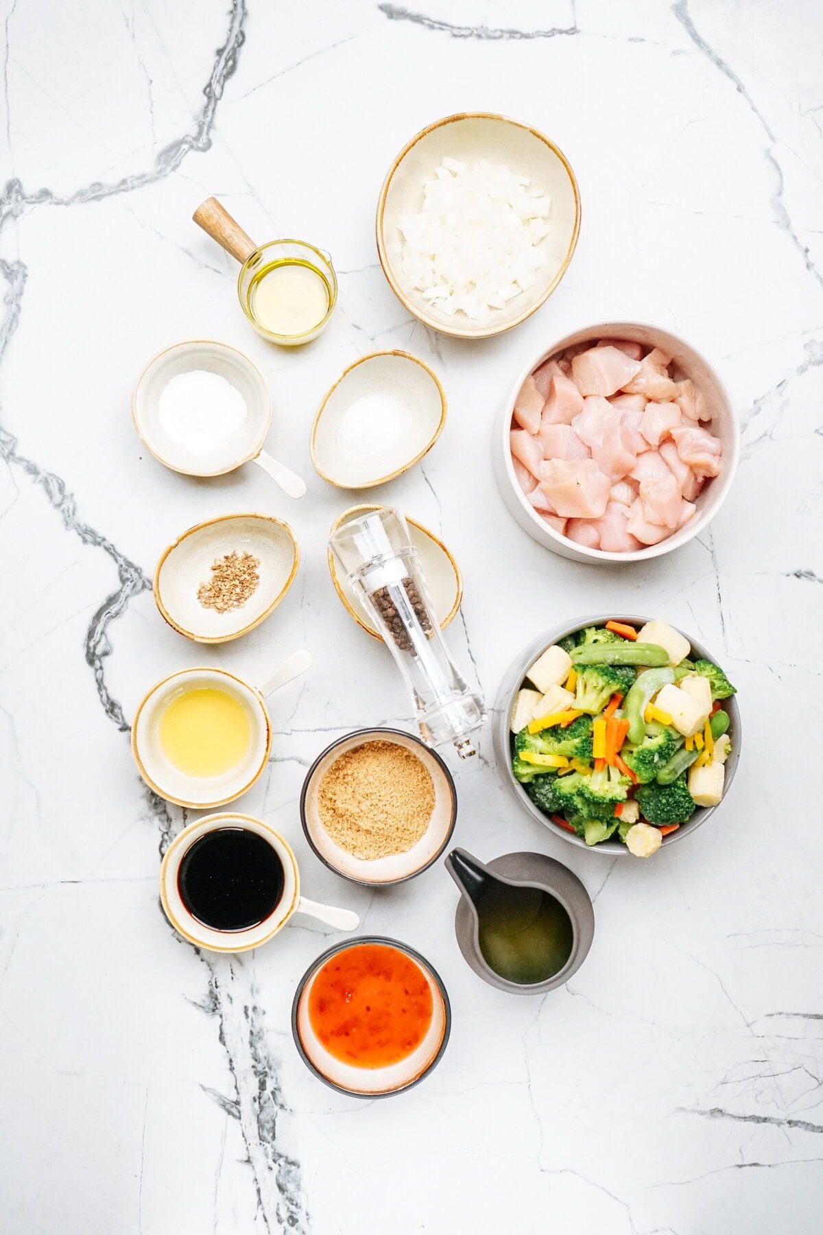 Ingredients for a stir fry recipe, featuring diced chicken, mixed vegetables, sauces, seasonings, and condiments, all artfully arranged on a marble surface.