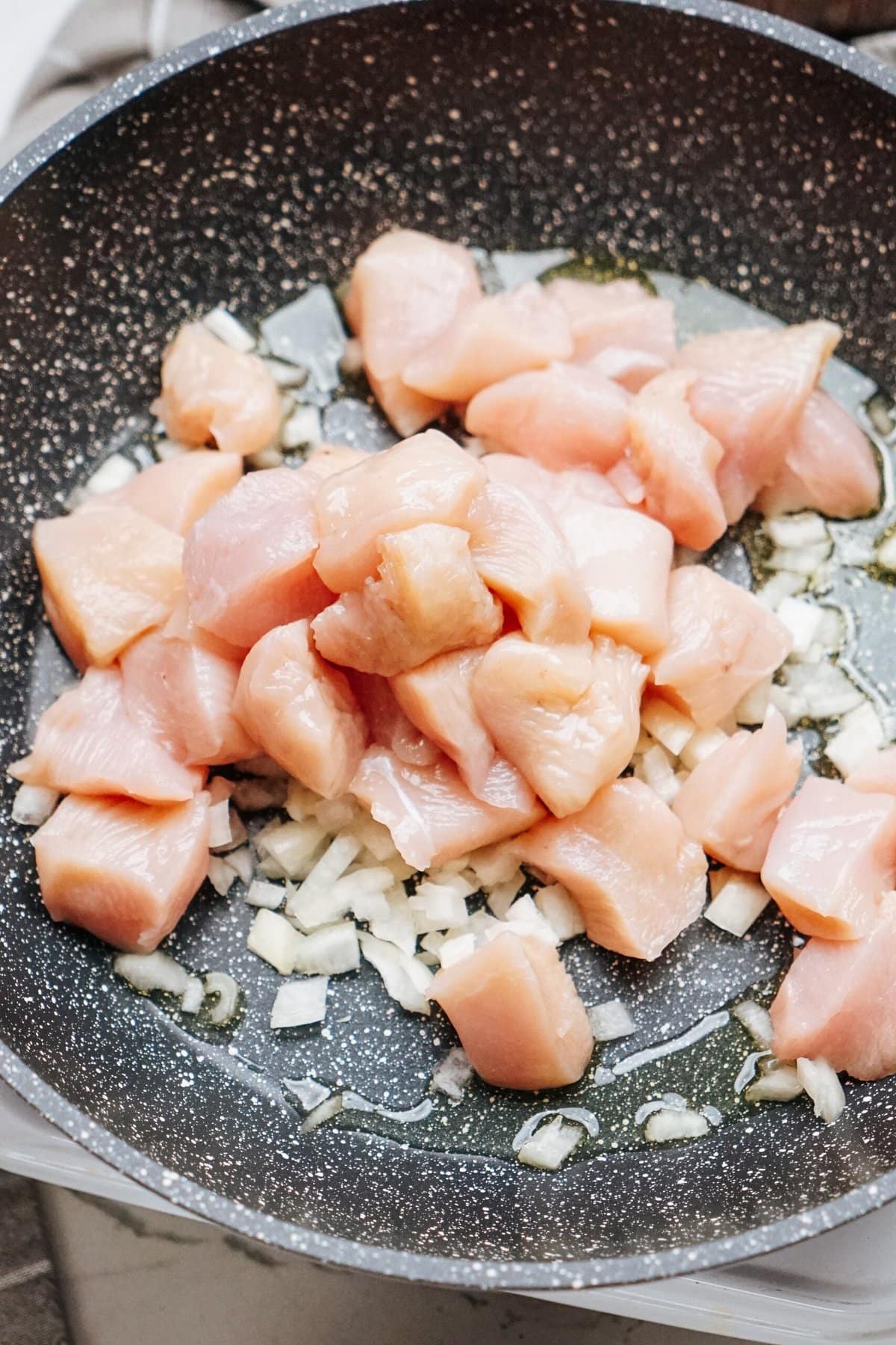 Diced raw chicken and chopped onions sizzle in a frying pan with a small amount of oil, creating the perfect base for a delicious stir fry.