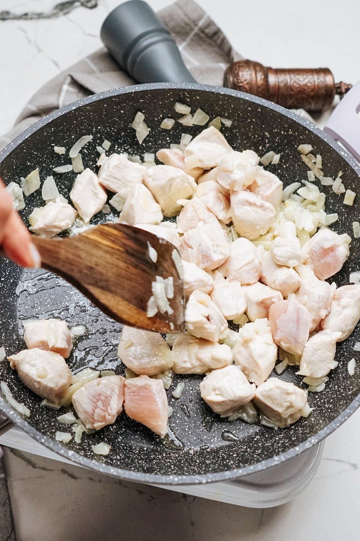 Diced chicken and onions are being expertly stir fried in a black pan with a wooden spatula, creating a tantalizing aroma.