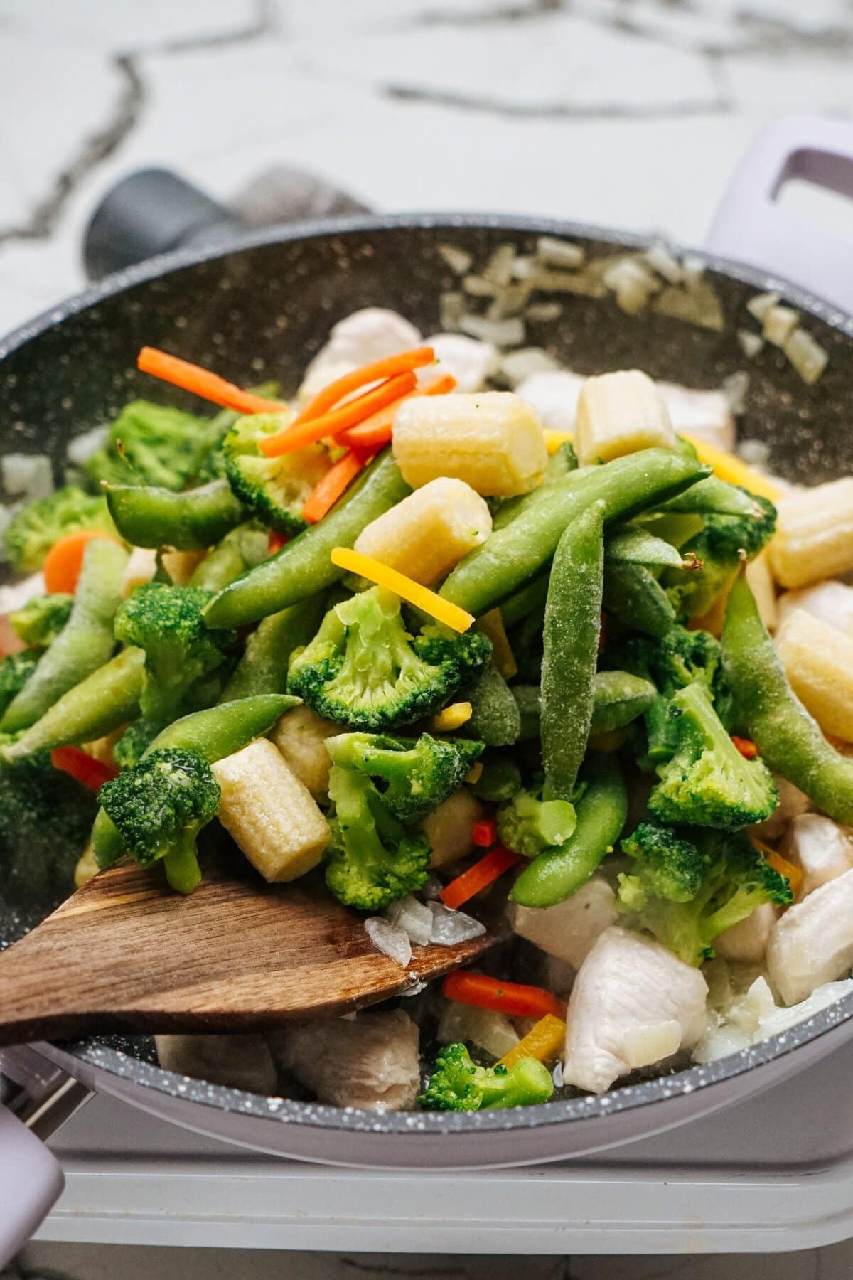 In a sizzling stir-fry, combine chicken, broccoli, snap peas, baby corn, and sliced carrots. Mix everything together with a wooden spatula for the perfect blend of flavors.