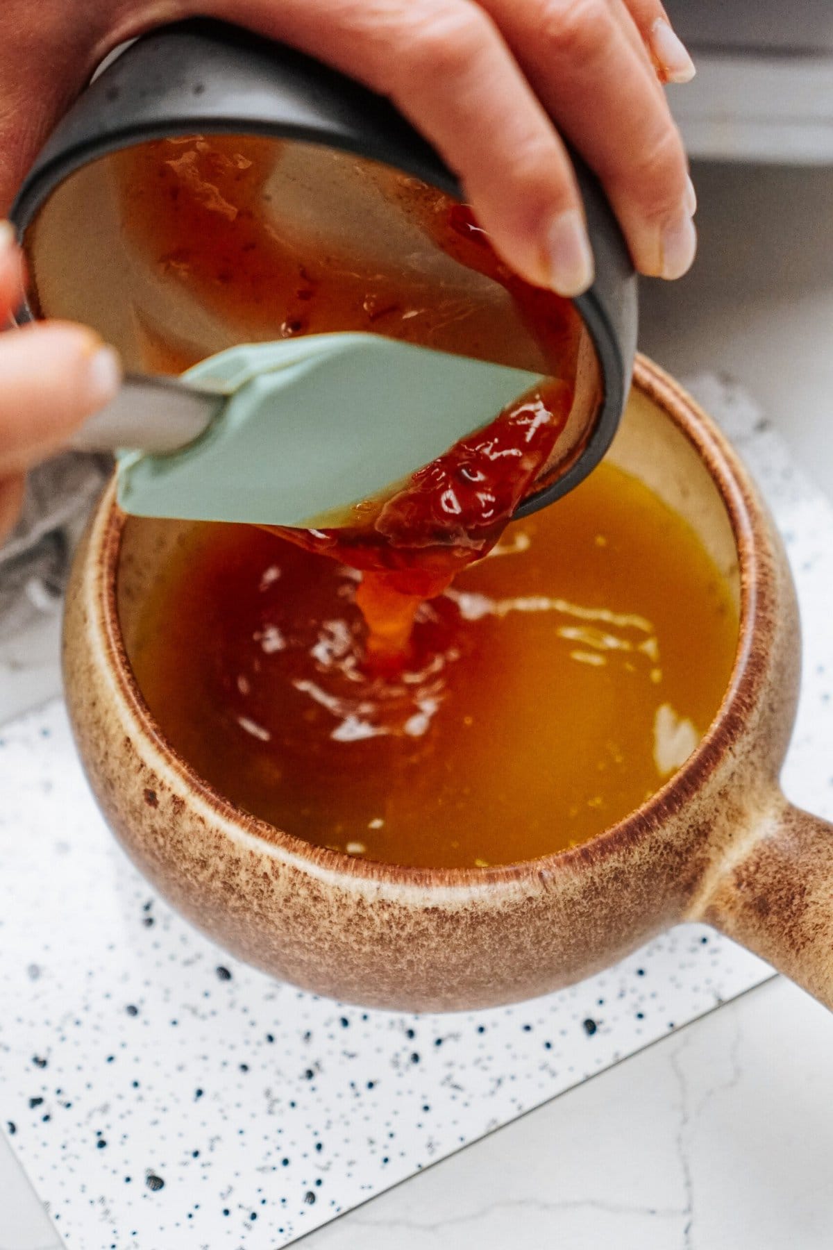 Hands pouring sauce from a small container into a bowl using a spatula, preparing the perfect stir fry.