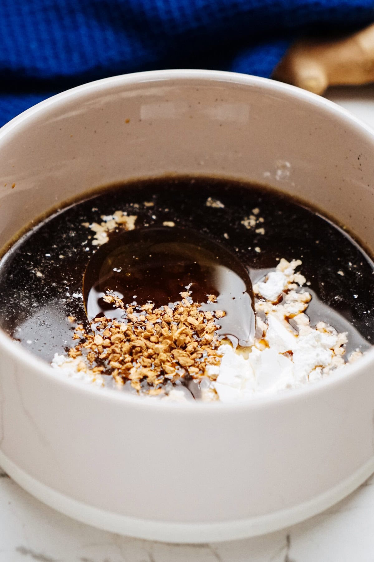 A bowl of dark liquid with white and brown ingredients on top, possibly instant coffee and creamer, evokes the allure of a rich stir fry sauce. A blue cloth provides a calming backdrop.