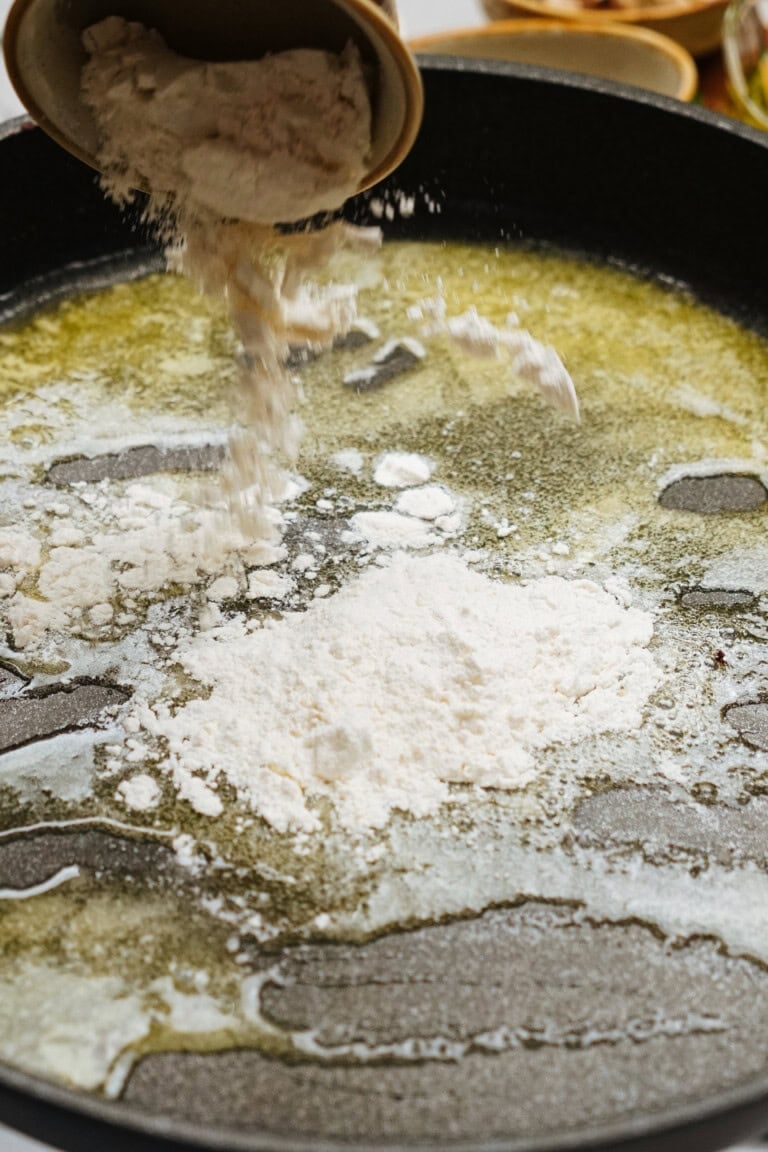 Flour is poured into a pan with melted butter, perhaps the first step in crafting a savory roux for a Salisbury steak recipe.