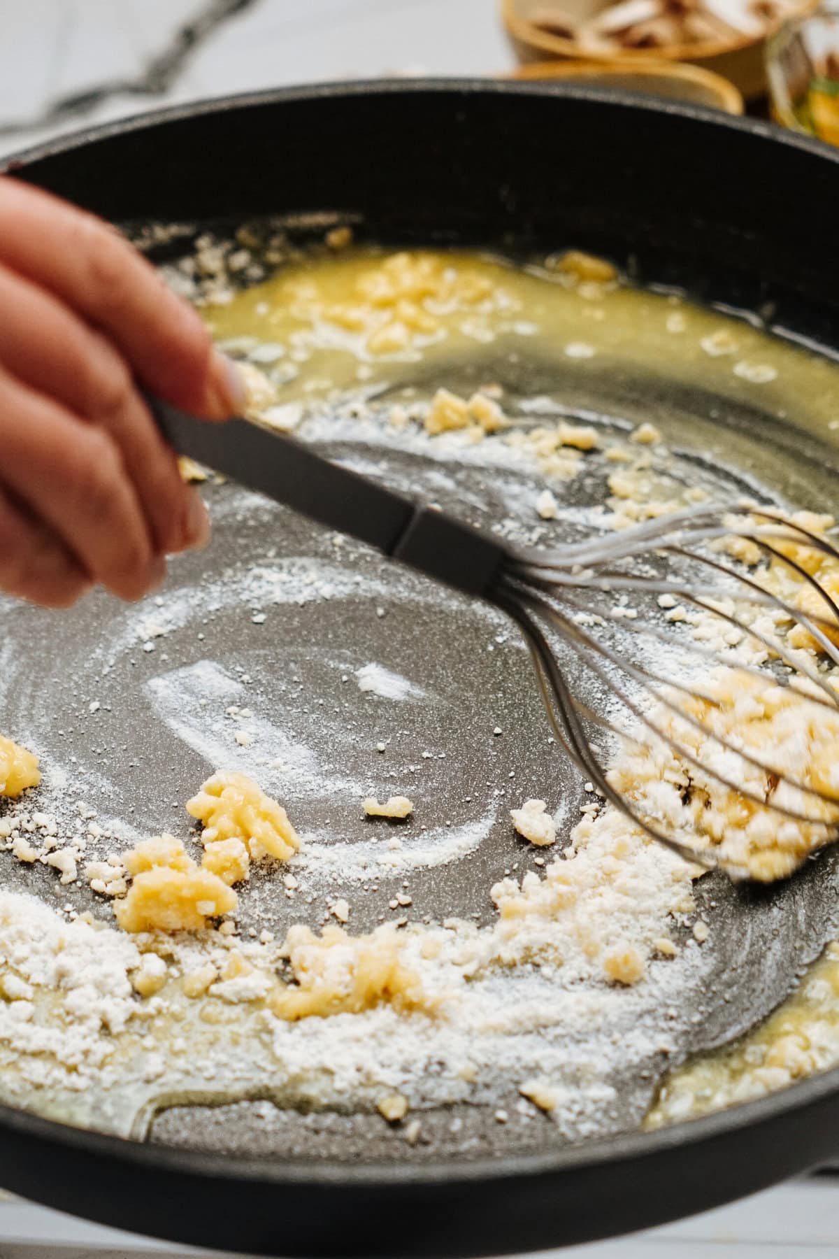 A hand using a whisk to stir flour and butter in a black frying pan, the beginning of a savory Salisbury steak recipe.