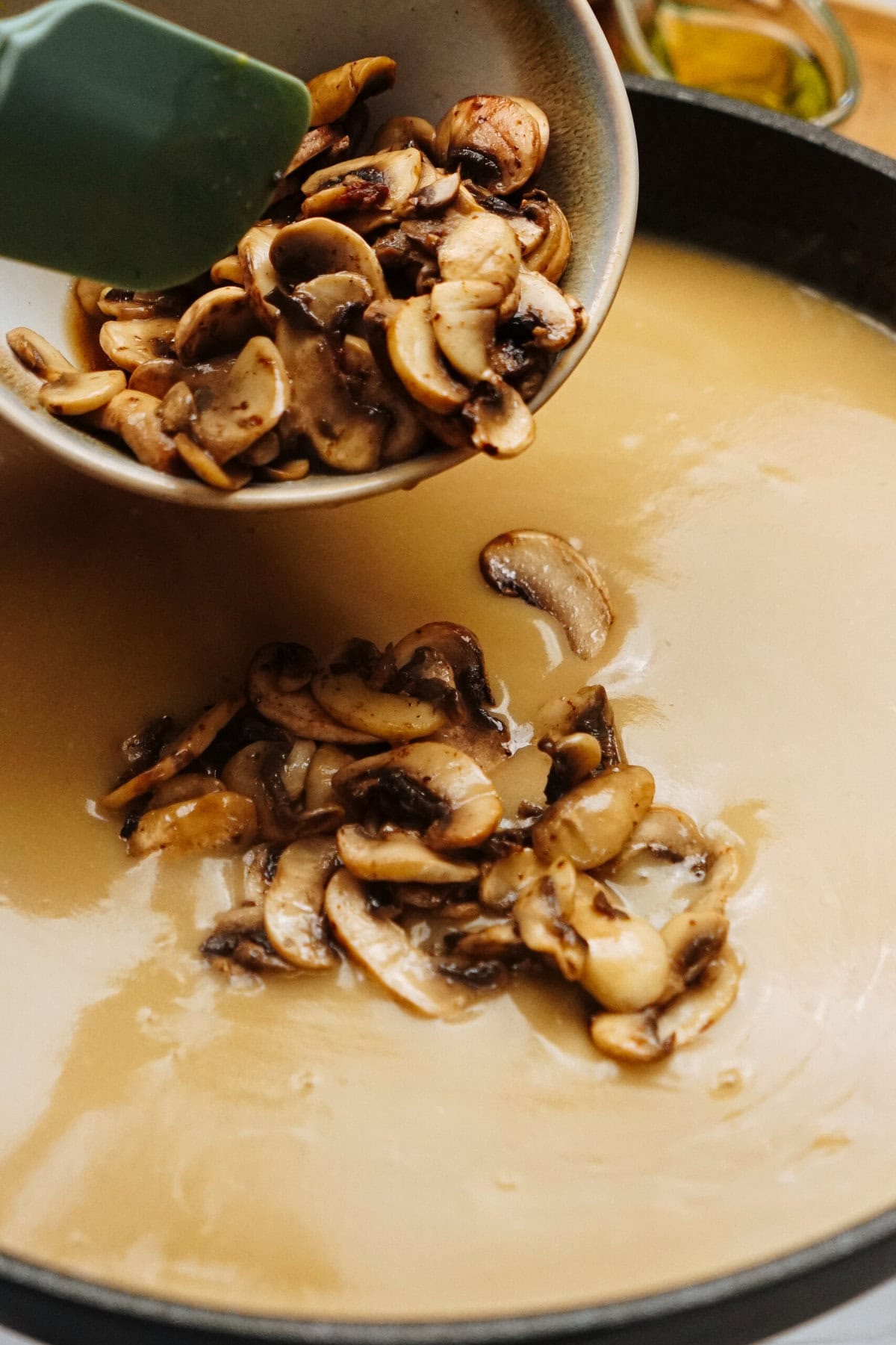 Sliced mushrooms are being added to a creamy sauce in a pan, creating the perfect base for a delicious Salisbury steak recipe.