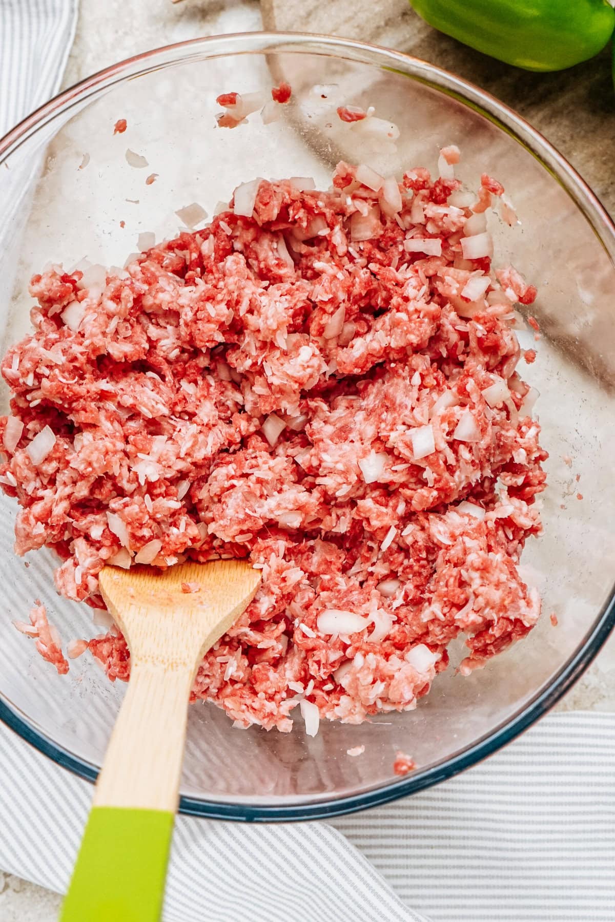 Ground meat mixed with chopped onions in a glass bowl, ready for filling those mouthwatering stuffed peppers, with a wooden spoon resting inside.