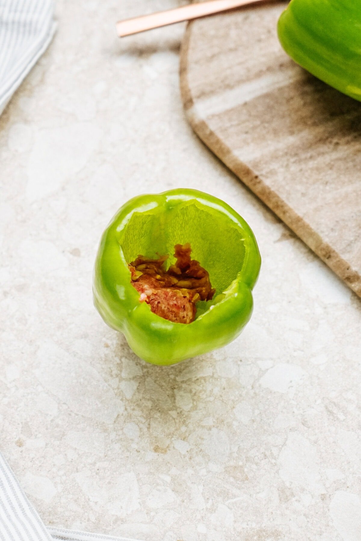 Stuffed peppers featuring green bell peppers brimming with savory brown rice and ground meat rest elegantly on a light stone surface.