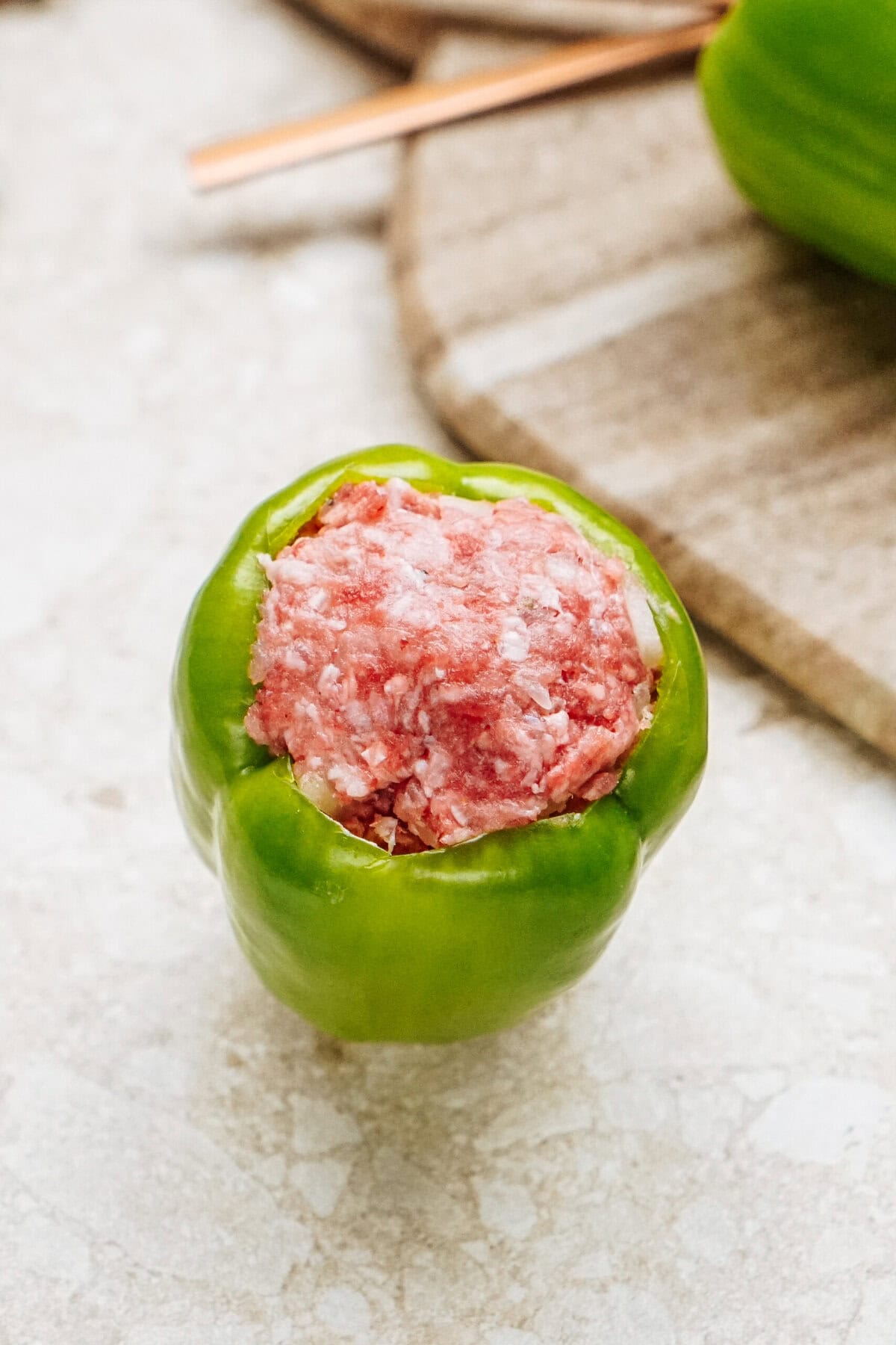 A delicious stuffed peppers dish featuring a green bell pepper filled with a savory ground meat mixture, all elegantly arranged on a light-colored surface.